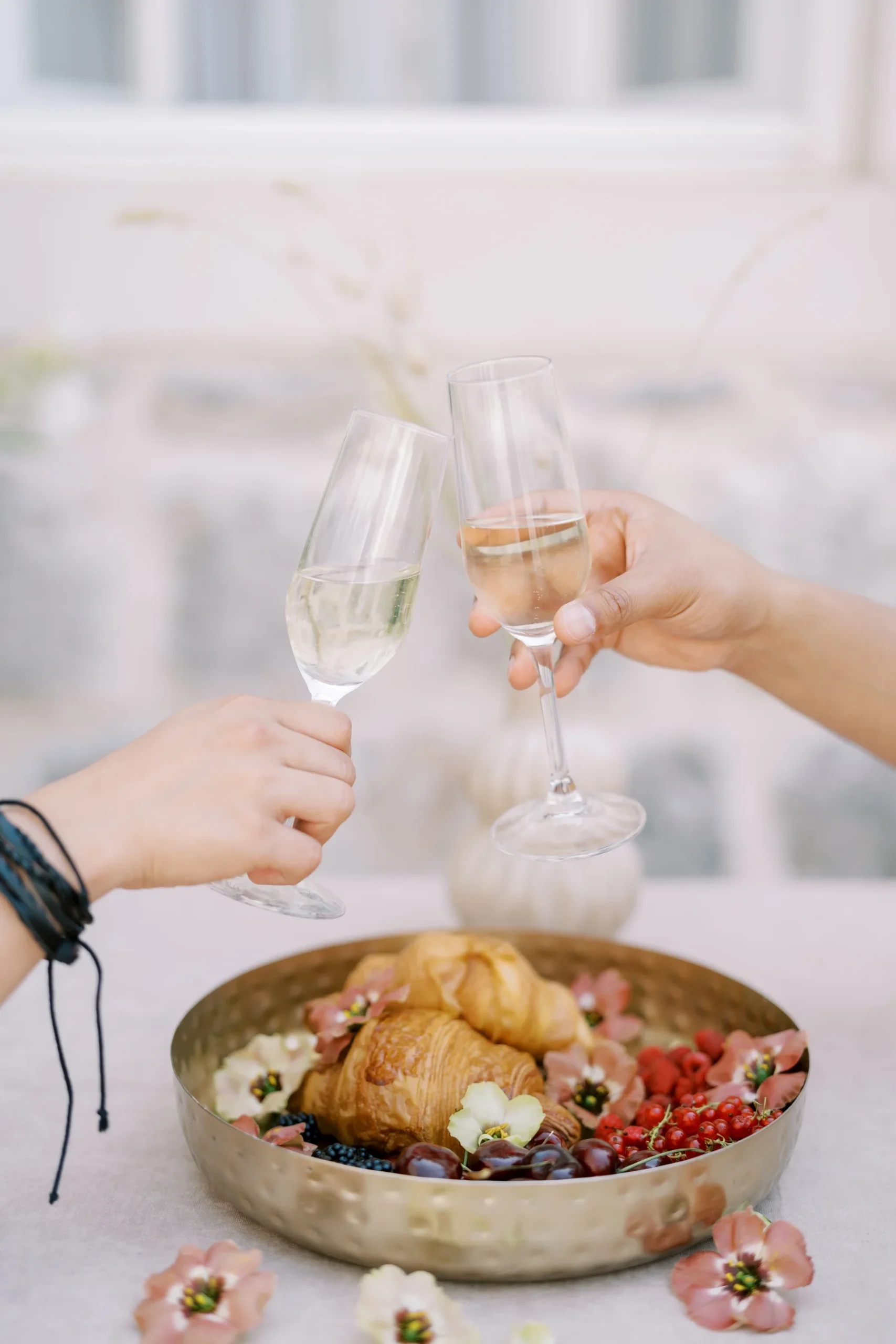 Two hands clink champagne flutes over a gold tray of croissants and berries at Monte Bay Retreat in Perast, Montenegro.