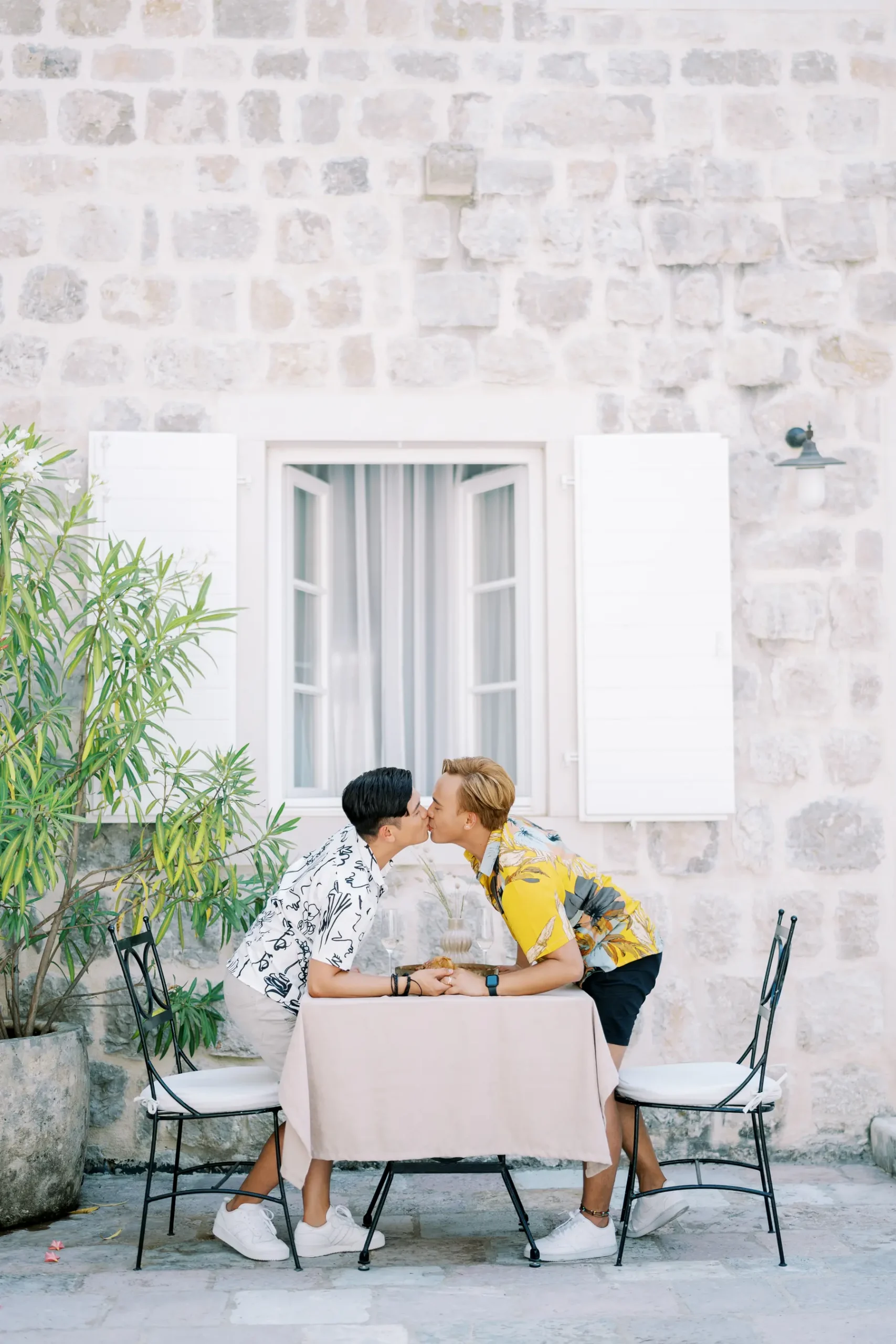 Ryan Jake Pisueña and Jori Blas Lazalita share a kiss at a cafe table outside Monte Bay Retreat in Perast, Montenegro.