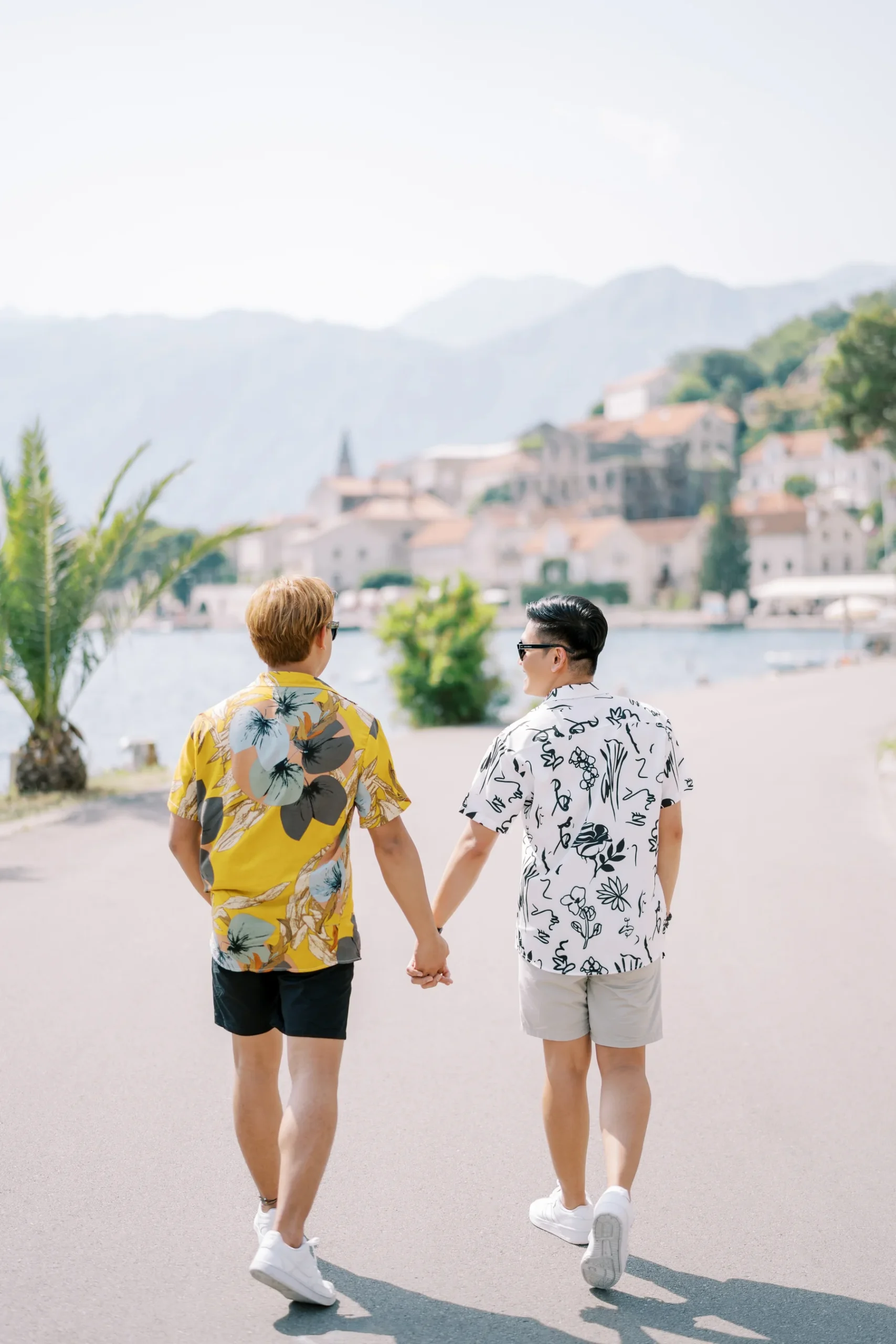 Ryan Jake Pisueña and Jori Blas Lazalita hold hands walking along the waterfront promenade in Perast, Montenegro.