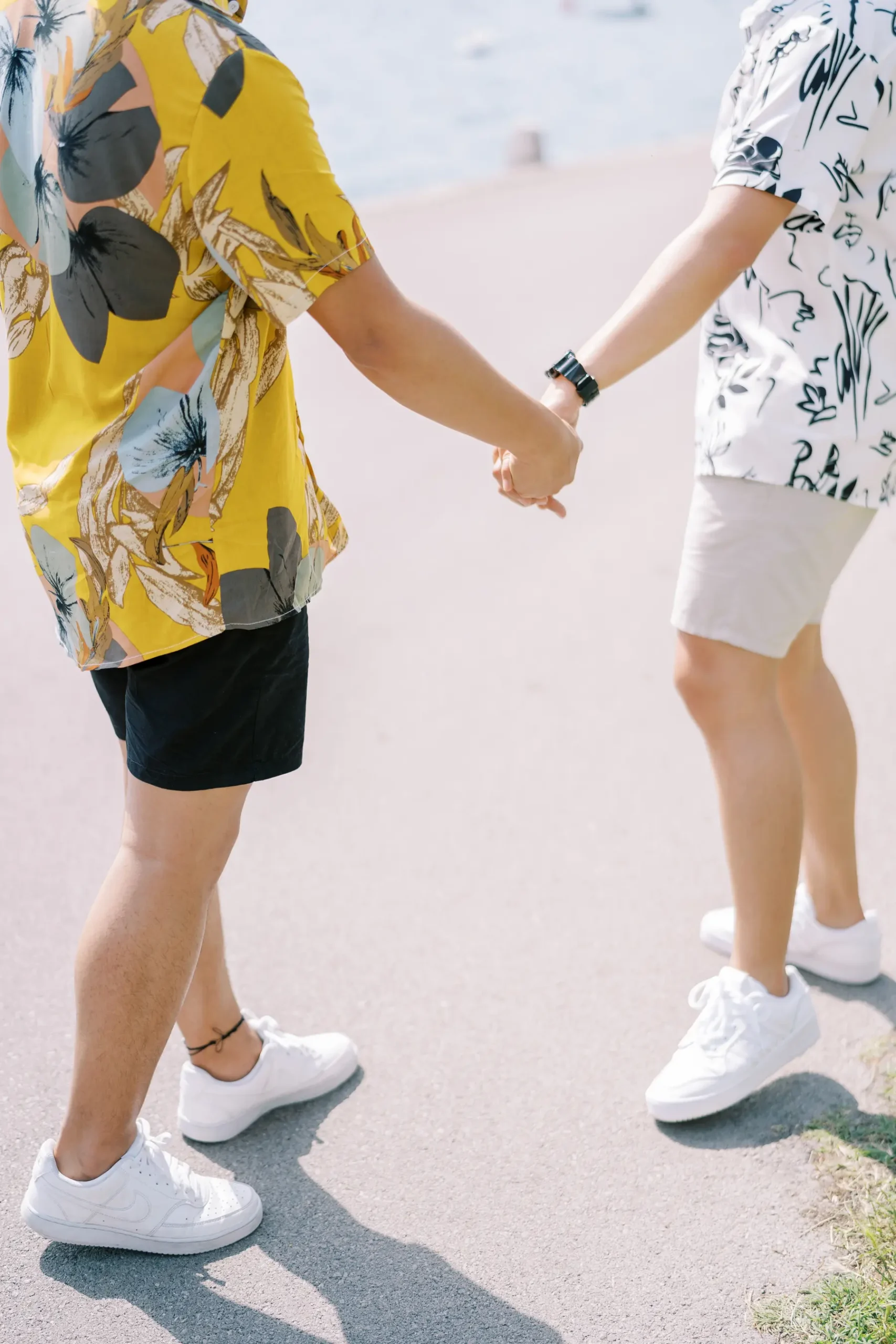Ryan and Jori hold hands while walking along a sunlit waterfront path in Perast, Montenegro.
