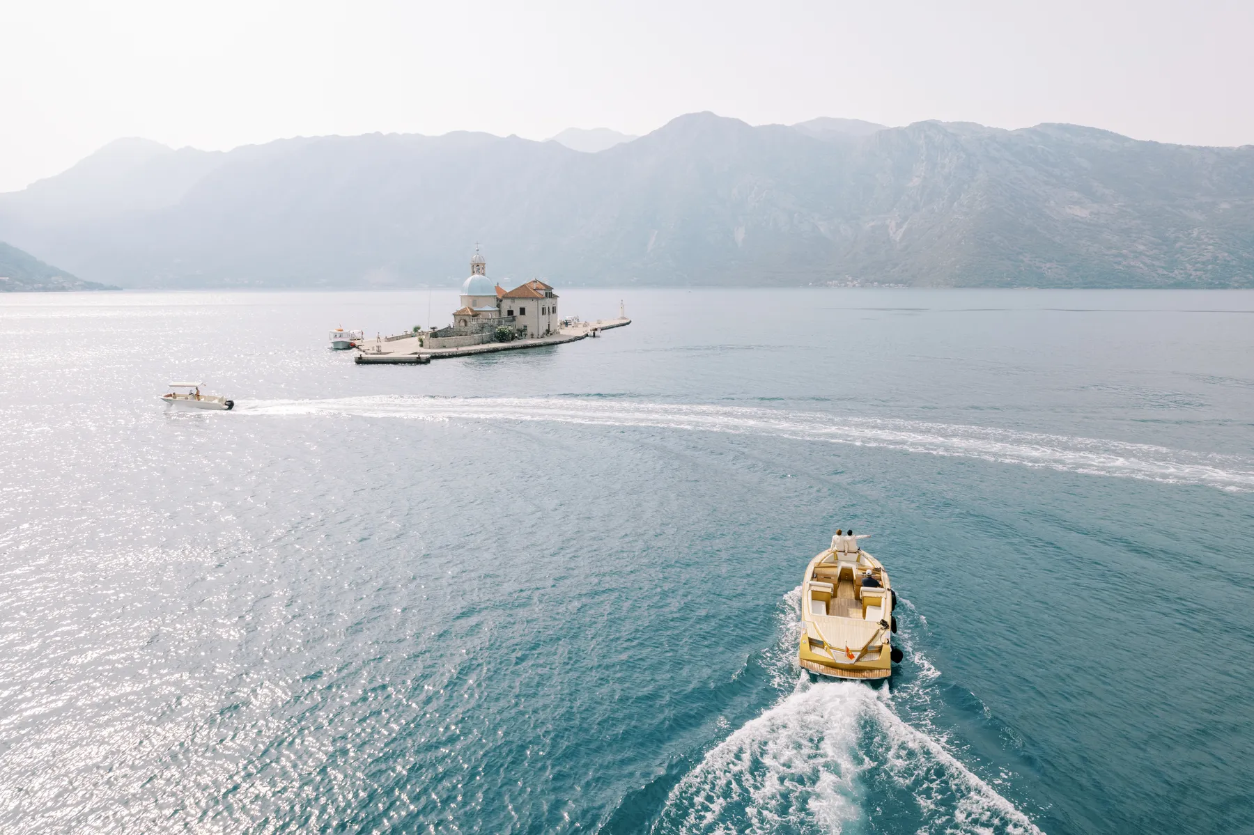 A gold yacht carries wedding guests across the Bay of Kotor toward Our Lady of the Rocks island in Perast, Montenegro.