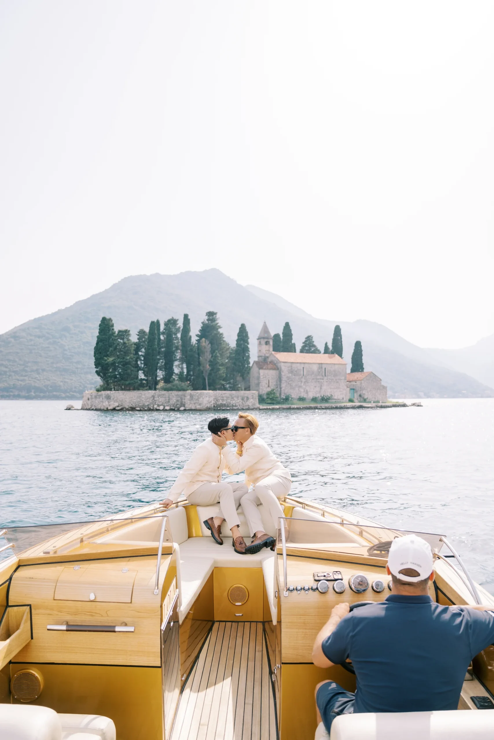 Ryan Jake and Jori Blas kiss on a wooden speedboat bow with St. George Island and Montenegro mountains behind them.