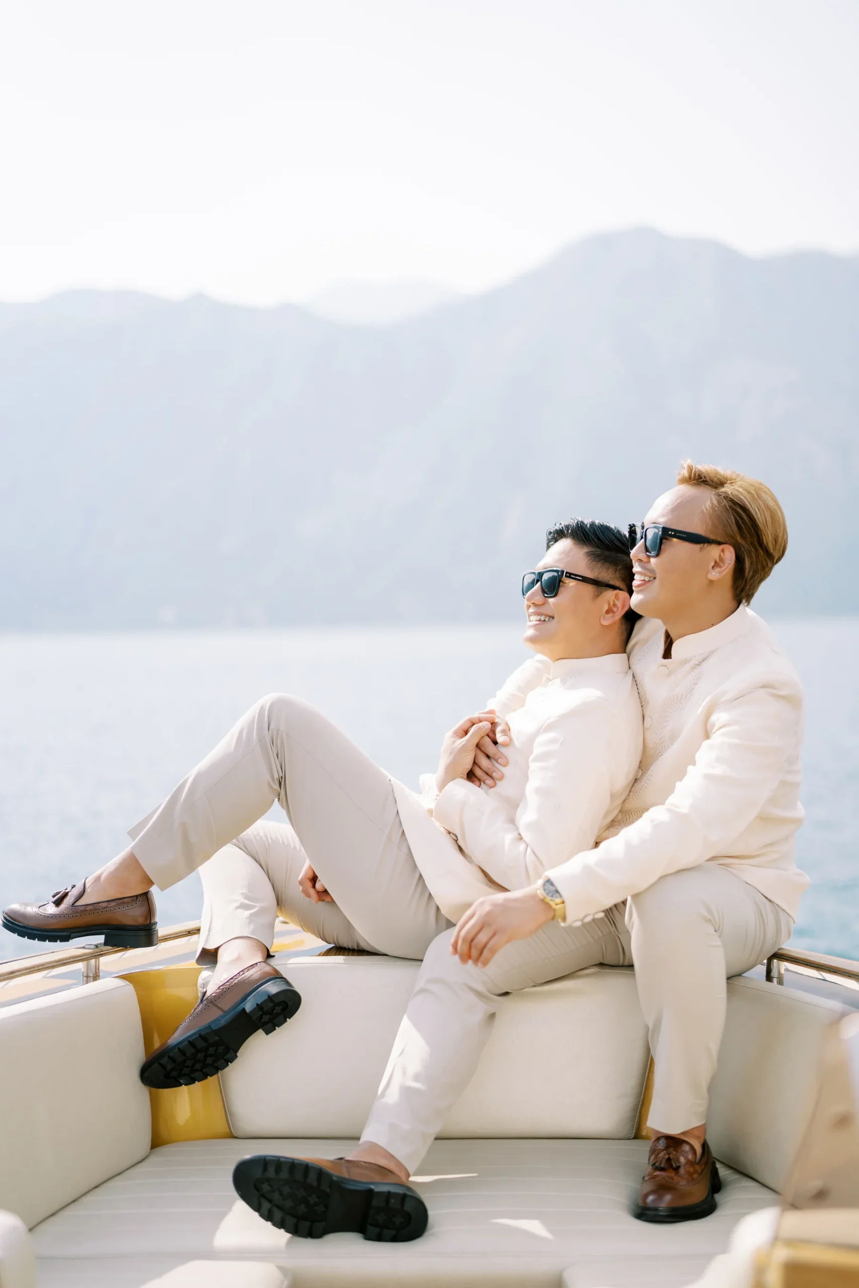 Ryan Jake and Jori smile aboard a yacht near Perast, Montenegro, wearing coordinating cream suits and sunglasses.