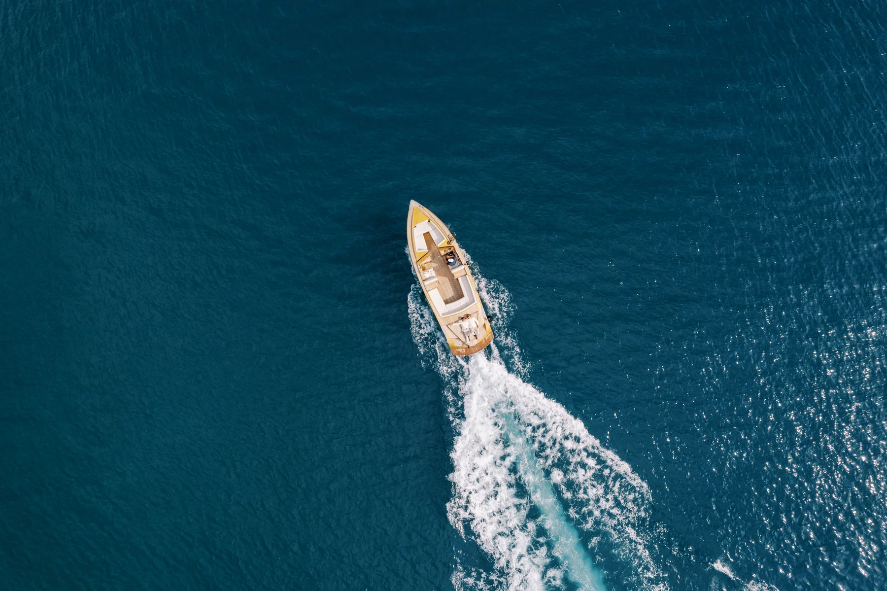 A luxury motorboat cuts through deep blue Adriatic waters near Perast, Montenegro, leaving a white foamy wake.