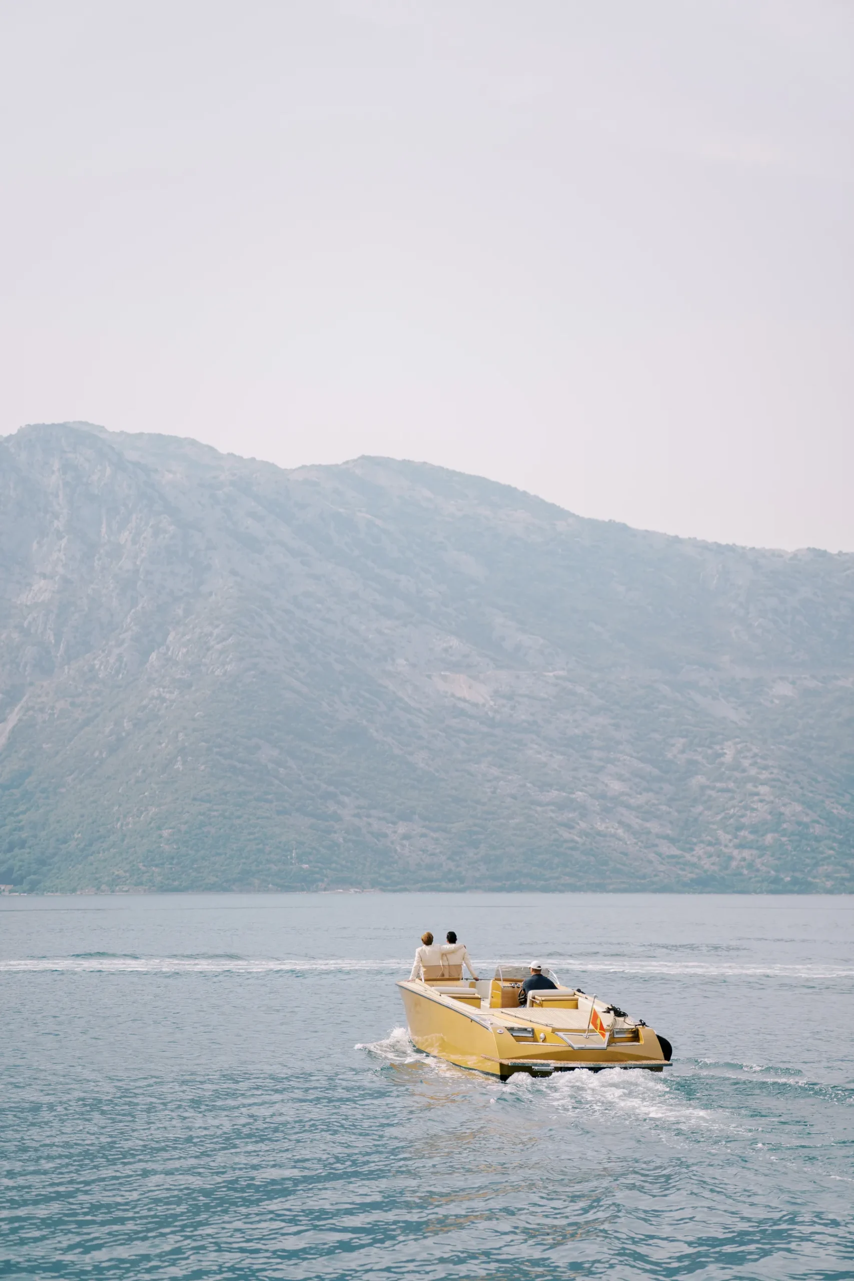 Ryan and Jori cruise a yellow motorboat across turquoise water with misty mountains behind them in Perast, Montenegro.