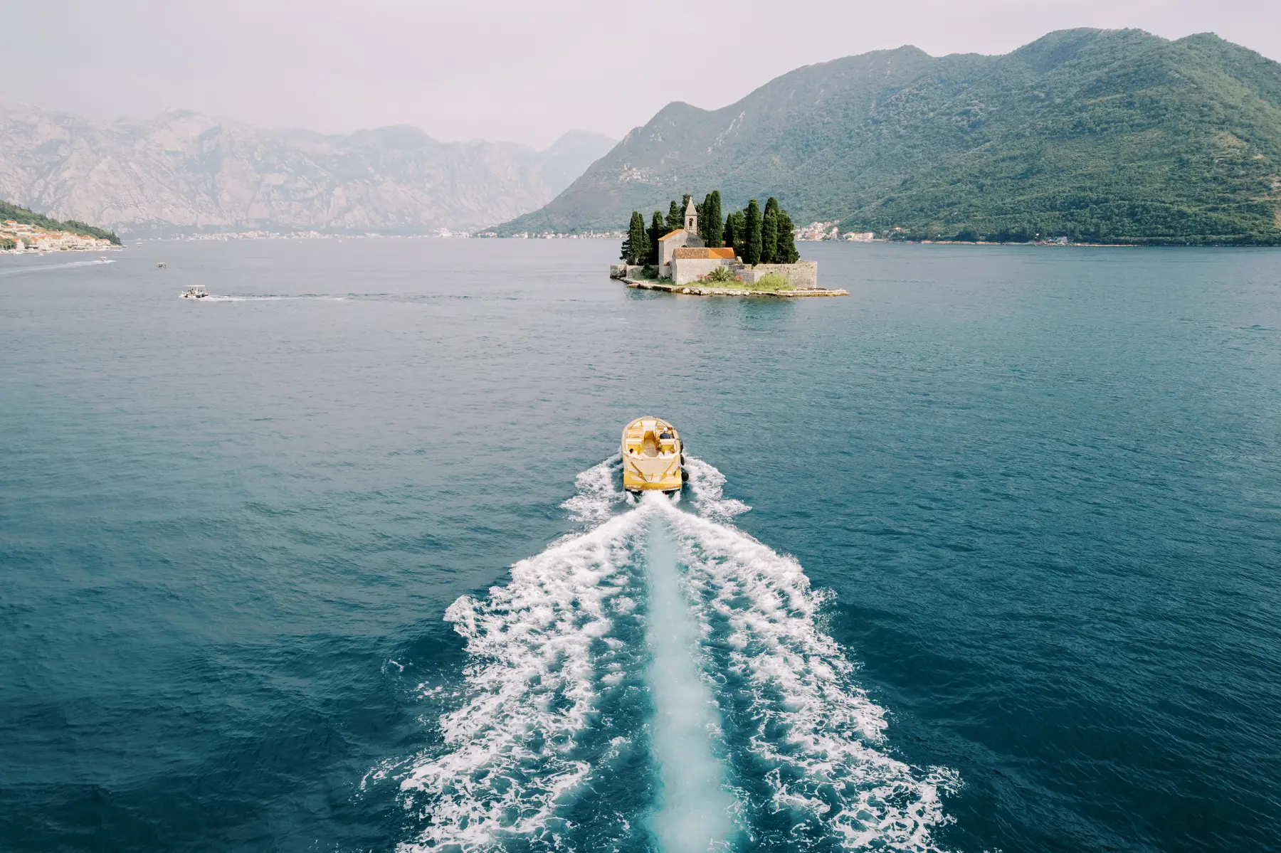 A yellow speedboat cuts across the Bay of Kotor toward St. George Island near Perast, Montenegro.