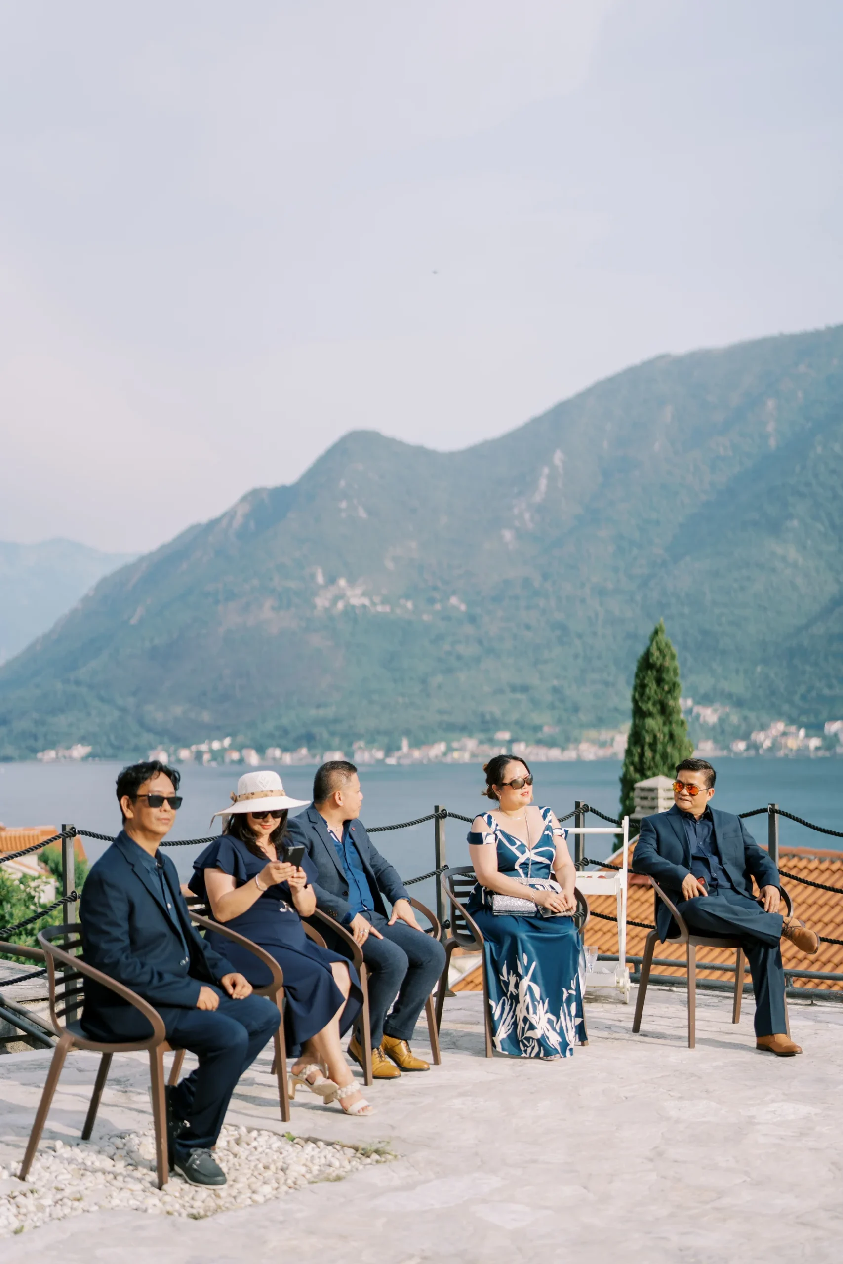Wedding guests in navy attire sit on a terrace overlooking the Bay of Kotor at Monte Bay Retreat in Perast, Montenegro.