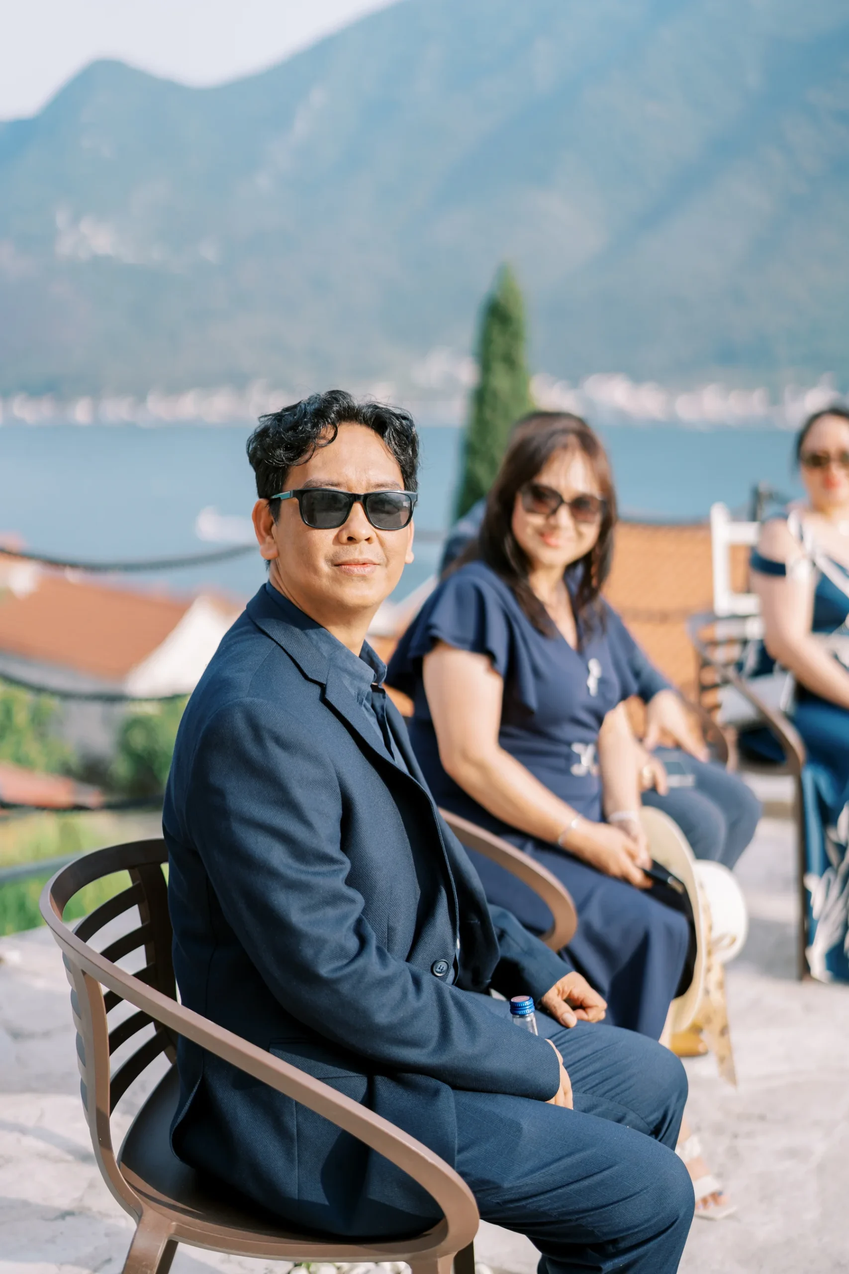 Wedding guests in navy attire sit outdoors at Monte Bay Retreat in Perast, Montenegro, with mountain and bay views.