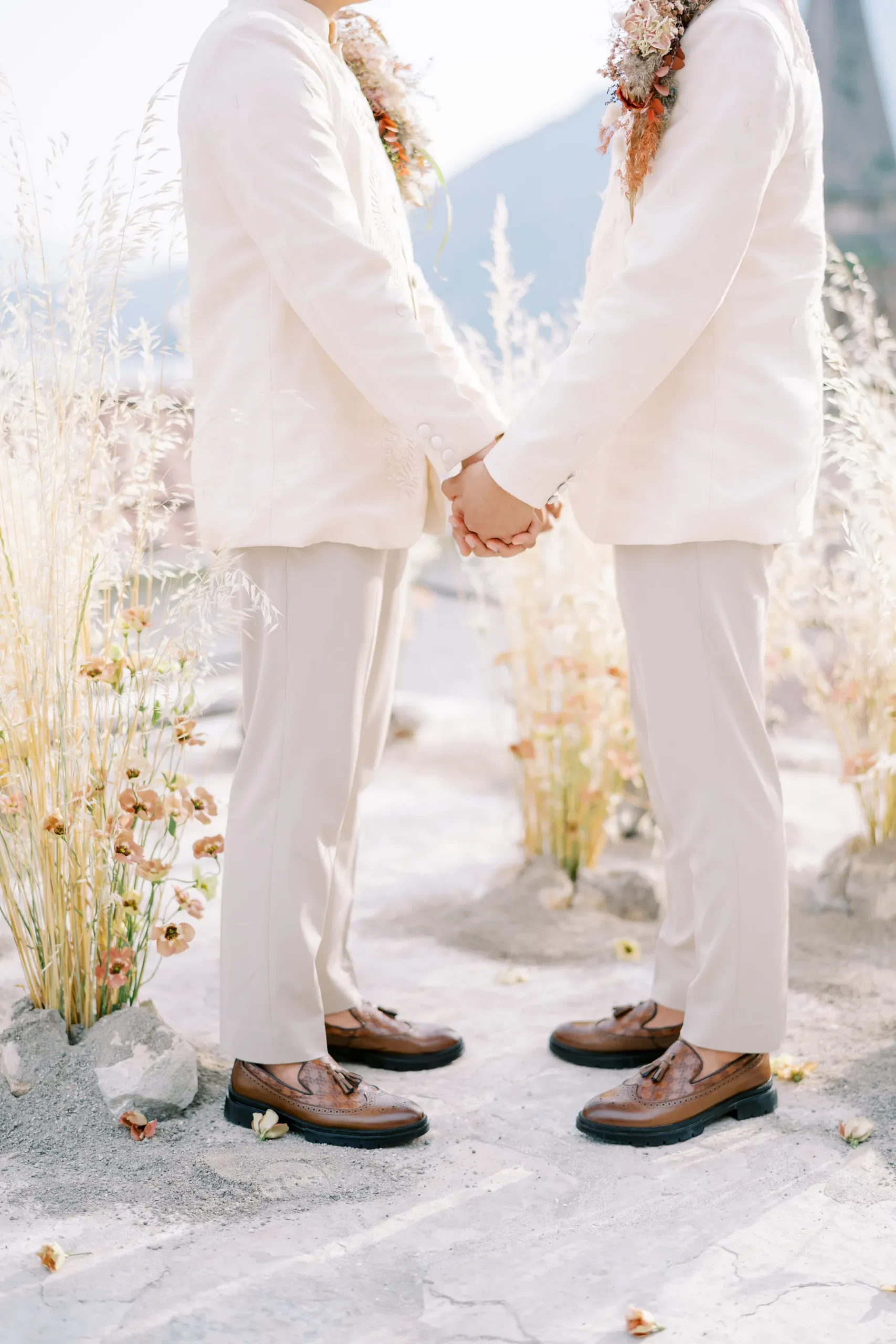 Ryan Jake and Jori hold hands in matching ivory suits and brown tassel loafers at Monte Bay Retreat in Perast, Montenegro.