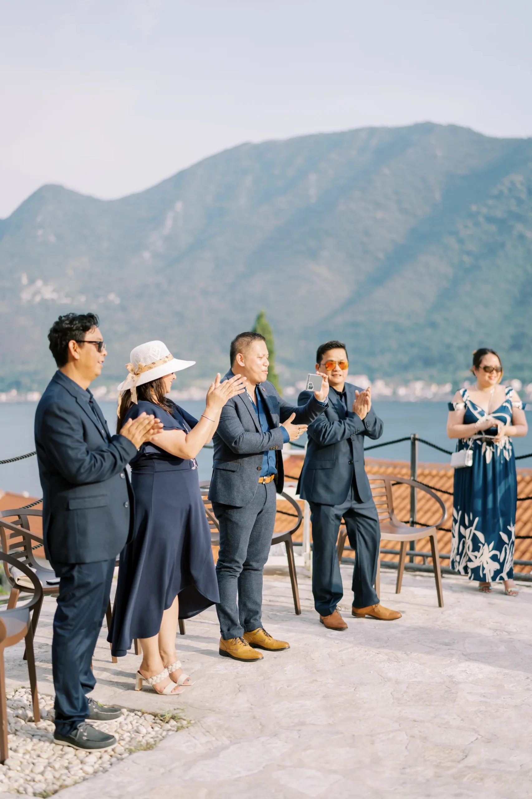 Wedding guests clap and celebrate outdoors at Monte Bay Retreat in Perast, Montenegro, with mountains and bay in the background.