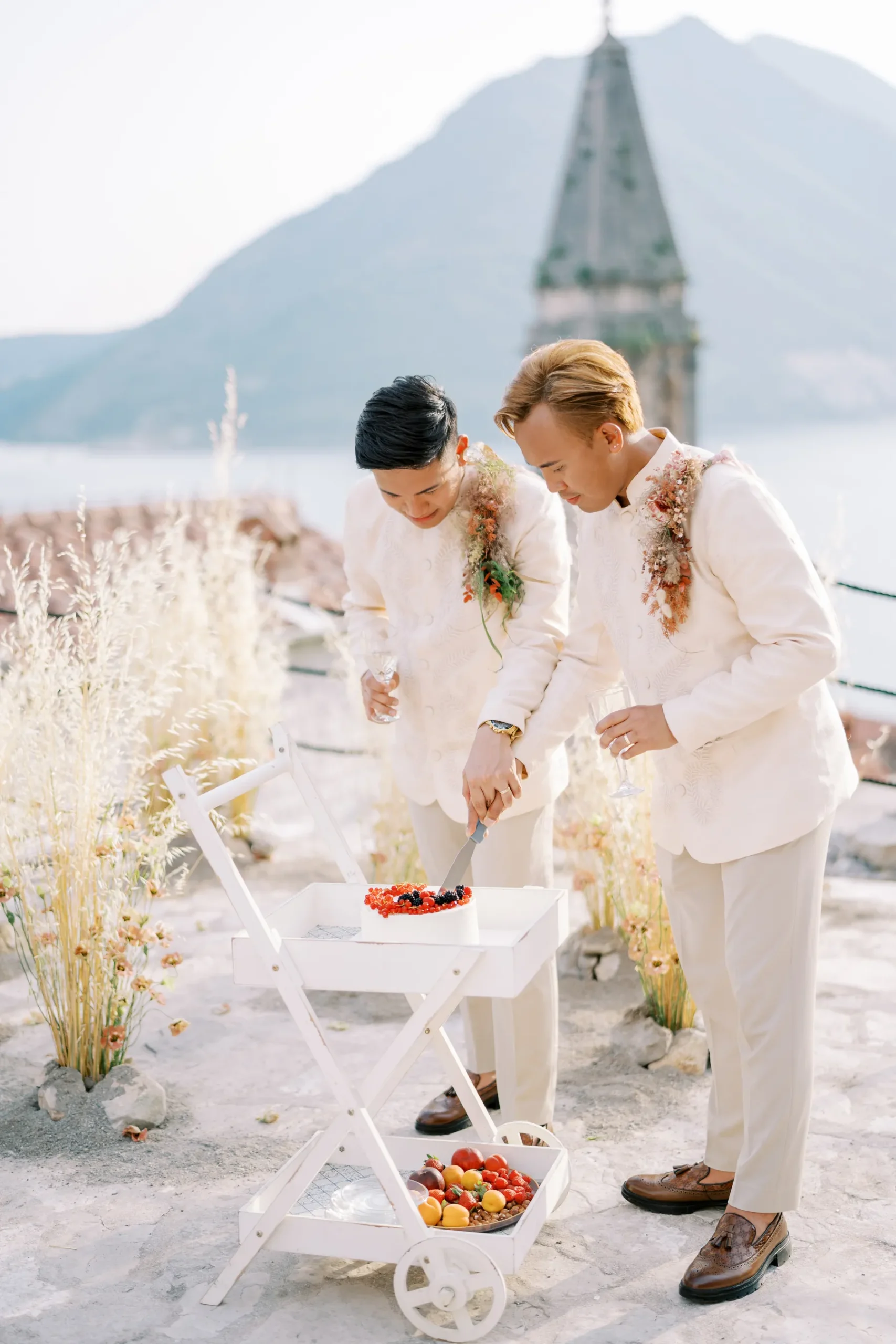 Ryan Jake and Jori cut their wedding cake on a white cart at Monte Bay Retreat in Perast, Montenegro.