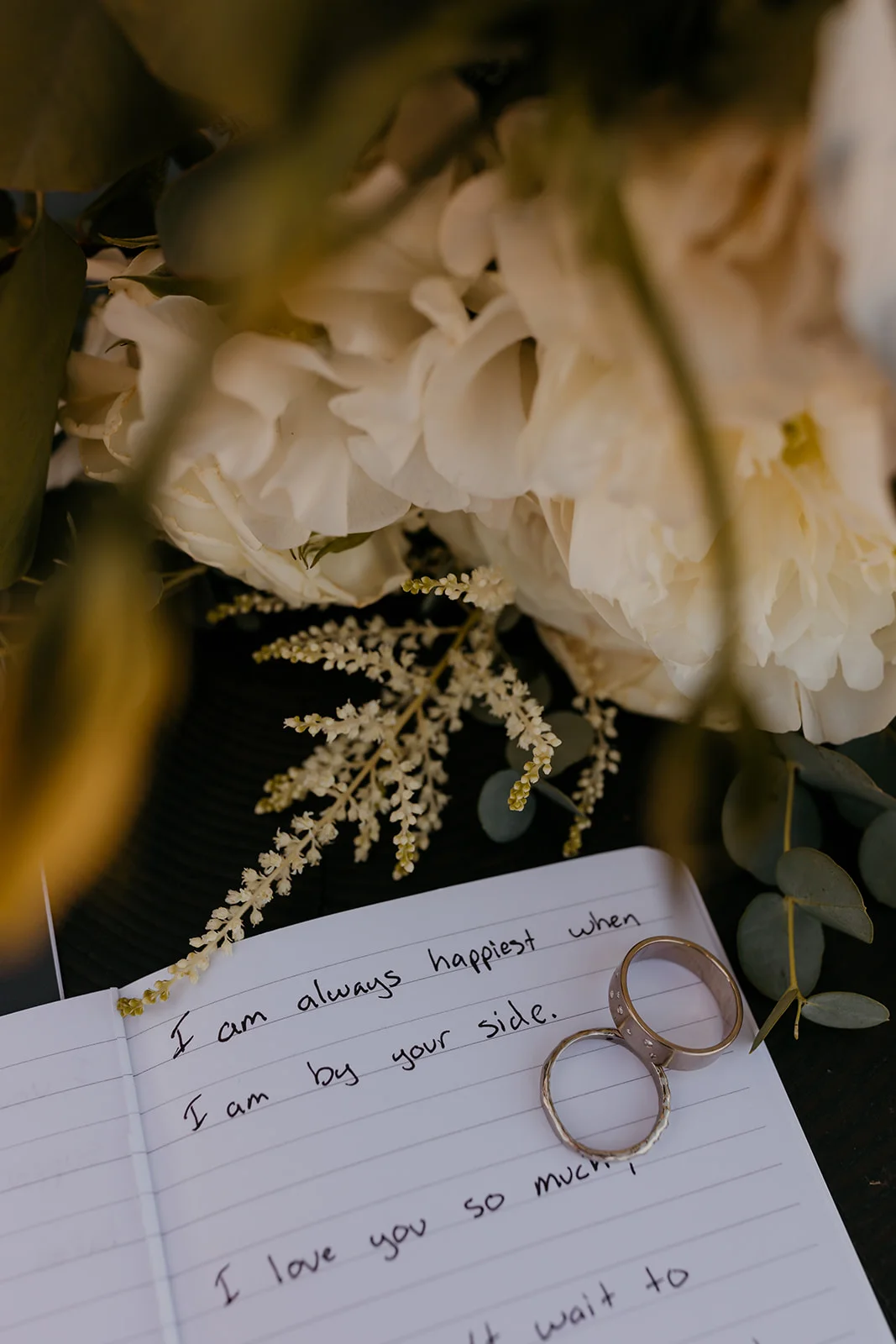 Wedding rings rest on handwritten vows beside white peonies and eucalyptus at Mayer State Park in Mosier, Oregon.