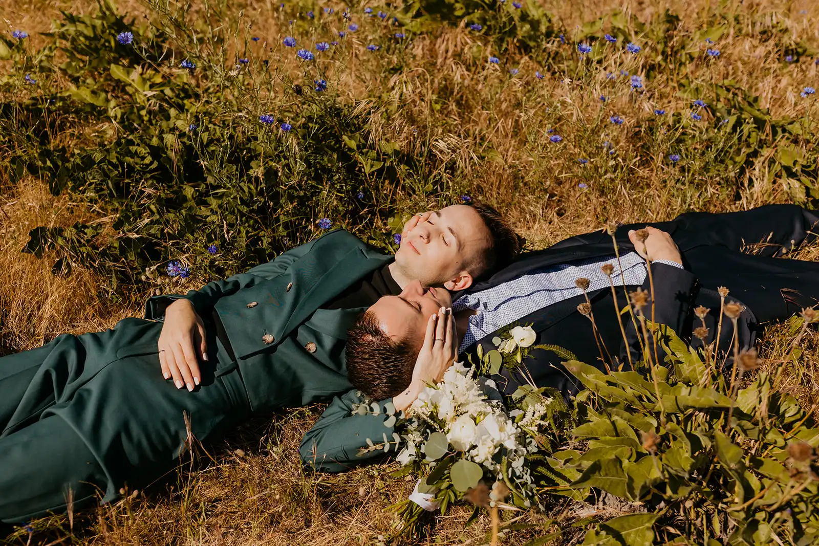 Ben and Nolan lie together in a wildflower meadow at Mayer State Park in Mosier, OR, holding a bouquet of white roses, peonies, sweet peas, astilbe and greenery.