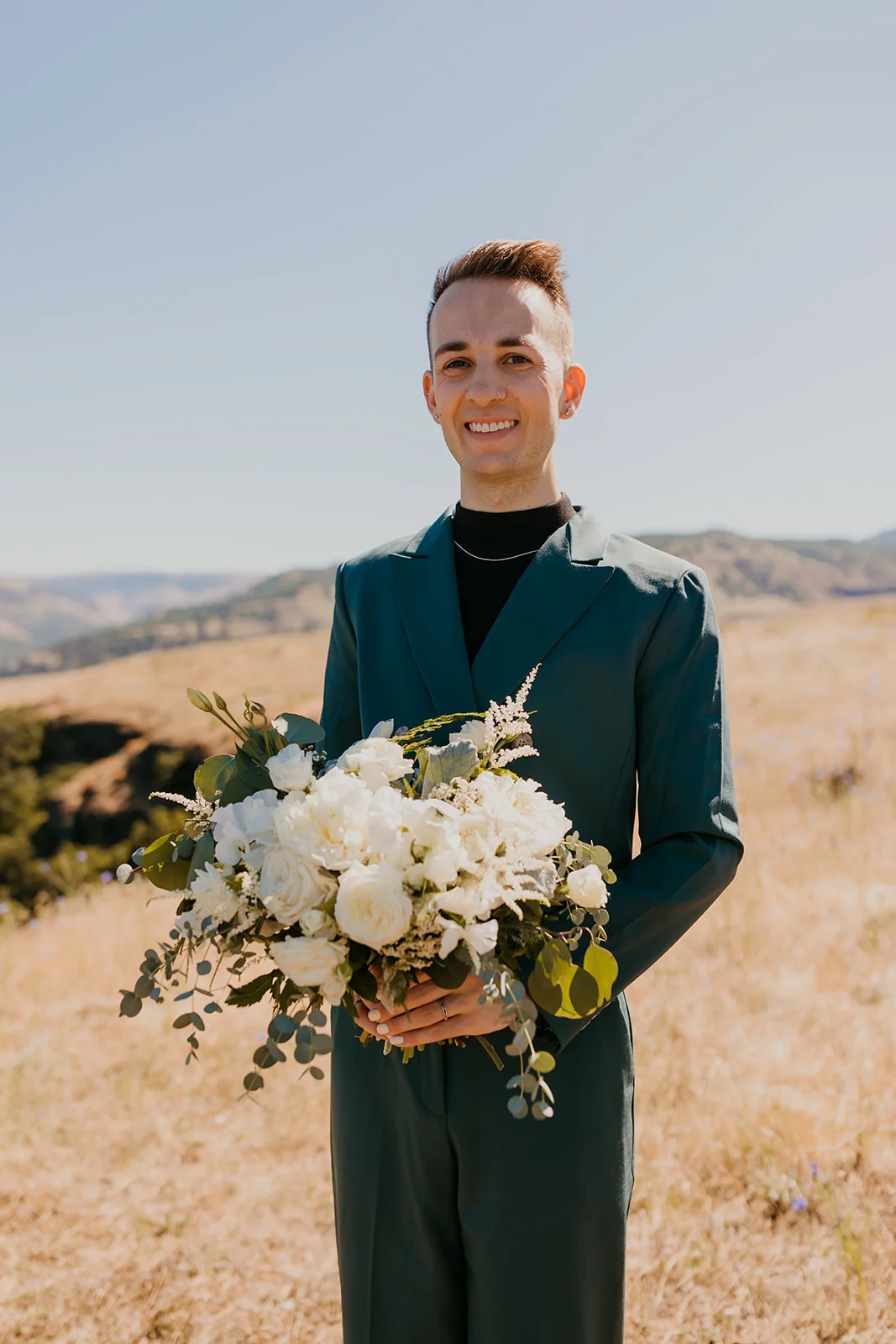 Nolan holds a lush white floral bouquet while standing in a golden field at NA Mayer State Park in Mosier, OR.