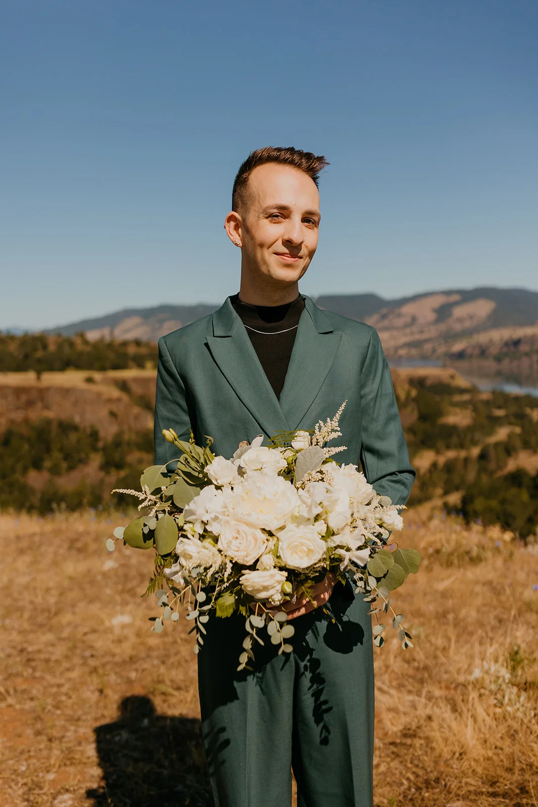 Groom holds a lush white floral bouquet in a teal suit at Mayer State Park in Mosier, OR.