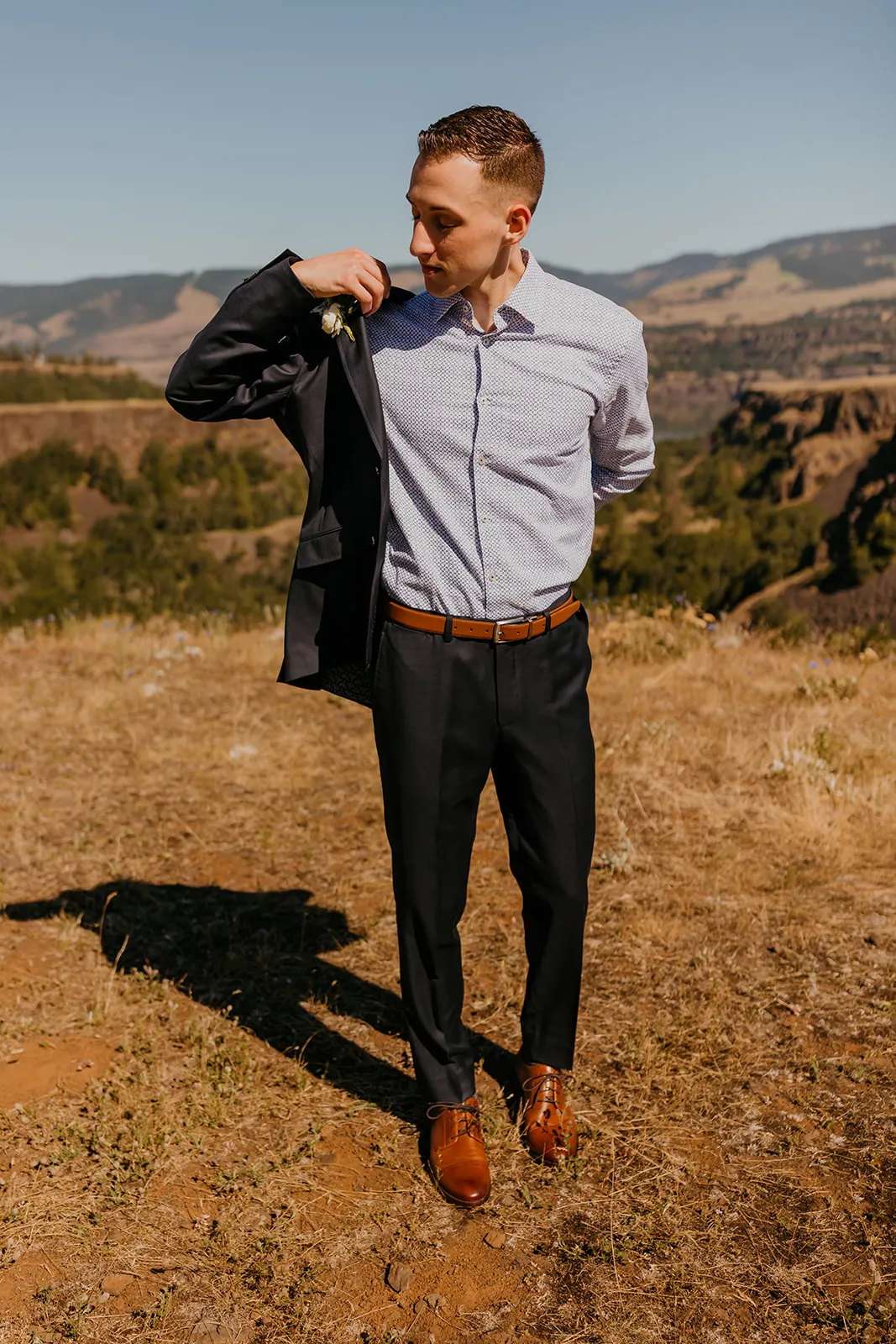 Groom Nolan slips on his navy blazer with boutonniere at Mayer State Park in Mosier, OR.