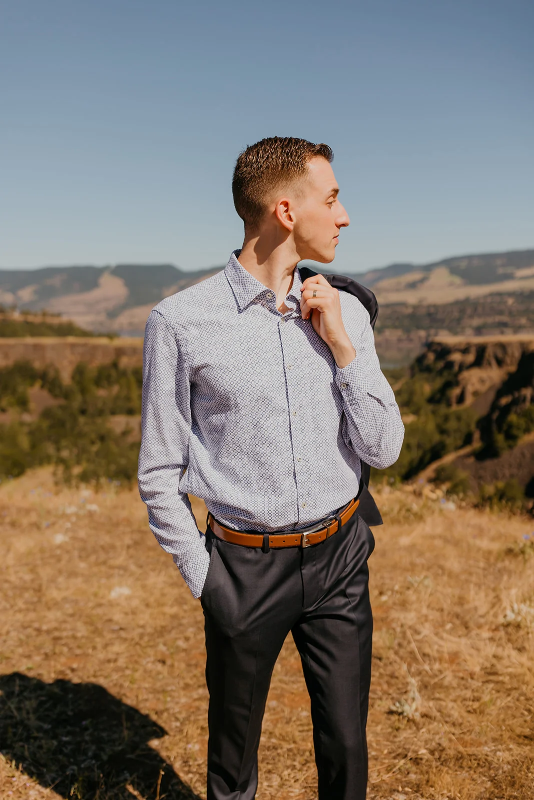 Nolan stands on a hilltop at NA Mayer State Park in Mosier, OR, holding his suit jacket over his shoulder.