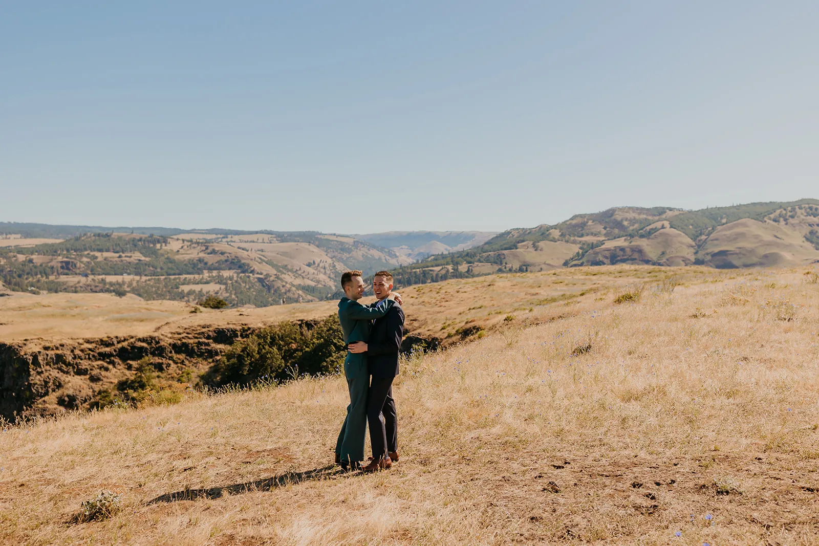Ben and Nolan embrace and laugh together on a golden hillside at Mayer State Park in Mosier, OR.