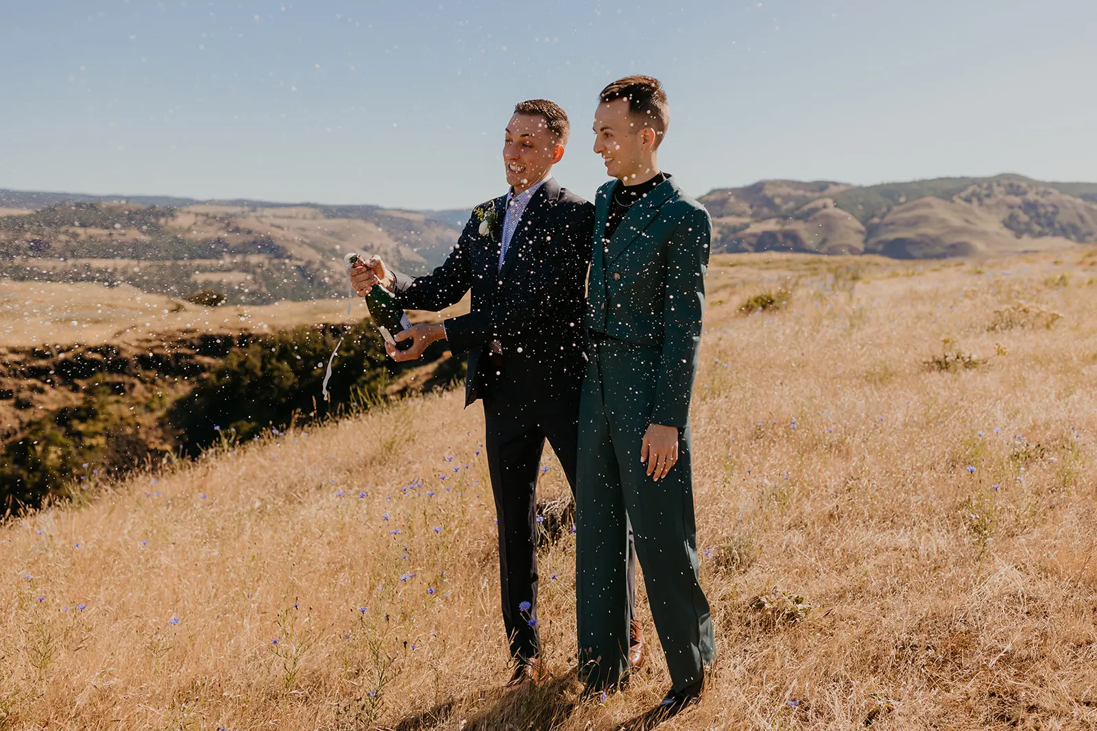 Ben and Nolan pop champagne on a golden hillside at Mayer State Park in Mosier, OR, sparkling droplets filling the air.