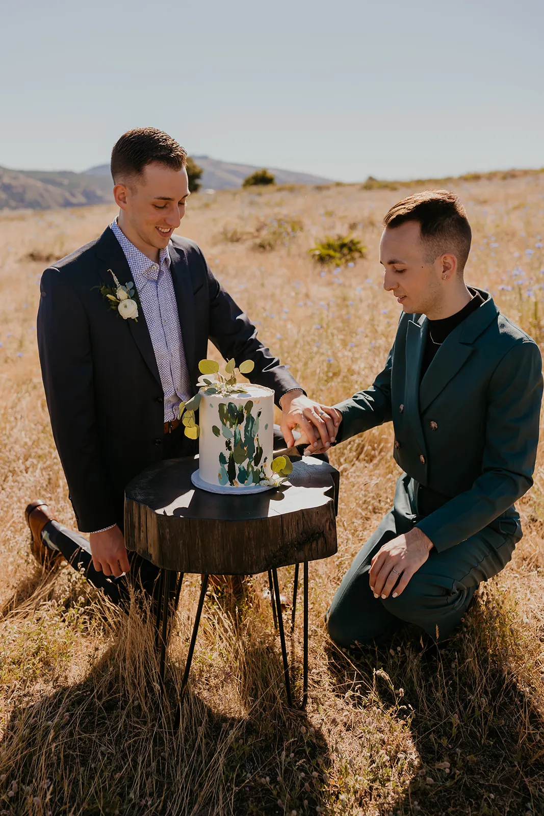 Ben and Nolan cut their botanical wedding cake on a wood stump table in a golden field at NA Mayer State Park, Mosier, OR.