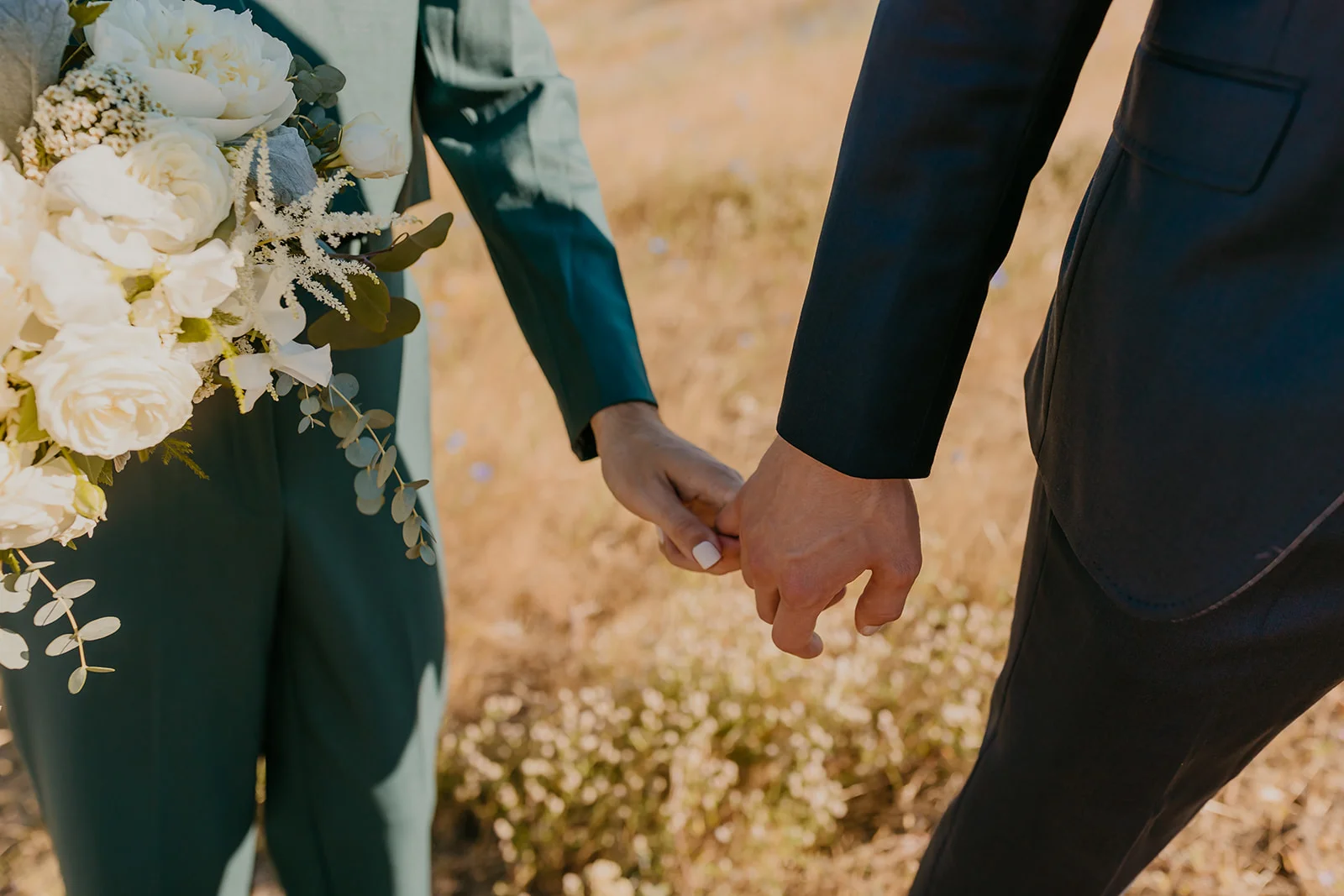 Ben and Nolan hold hands at Mayer State Park in Mosier, Oregon, one wearing a teal suit and carrying a white floral bouquet.