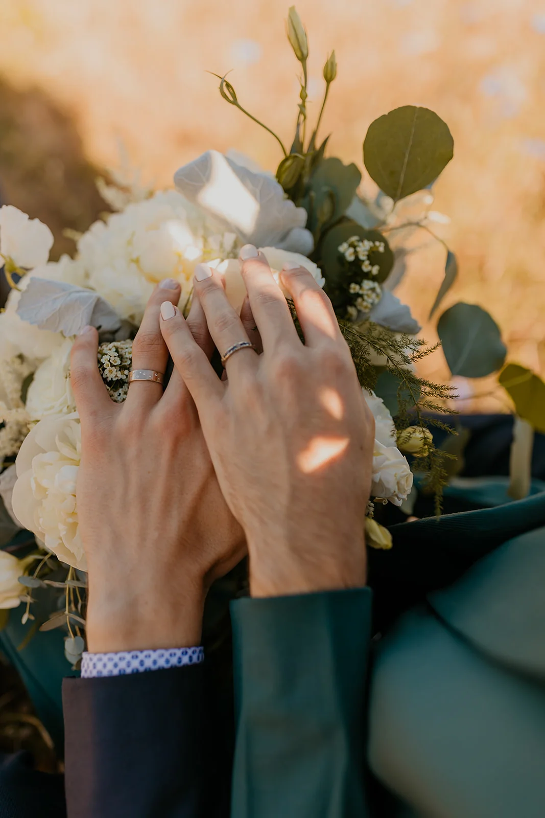 Ben and Nolan's hands rest on their white floral bouquet, wedding bands visible, at Mayer State Park in Mosier, OR.
