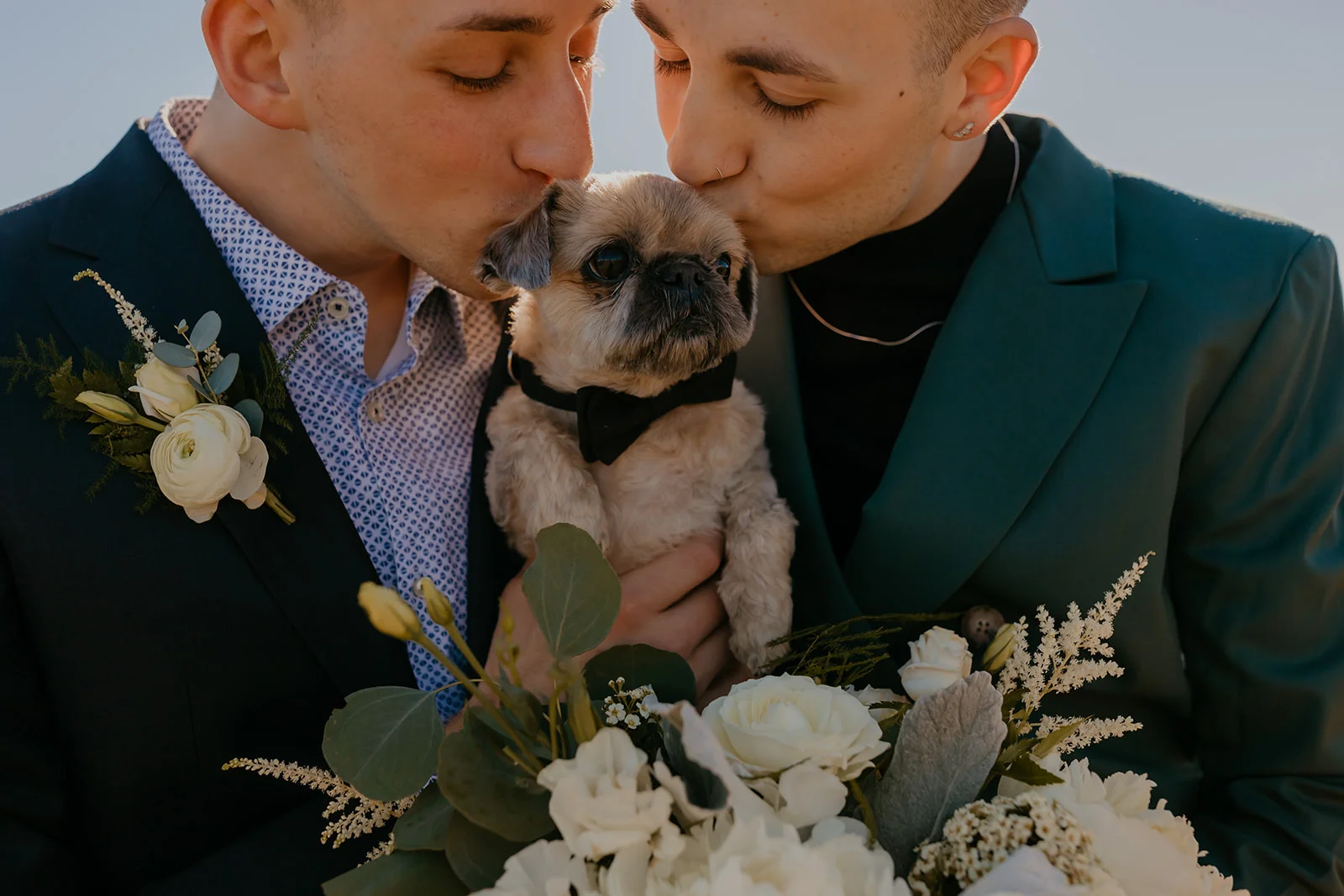 Ben and Nolan kiss their small dog dressed in a bow tie at Mayer State Park in Mosier, OR.