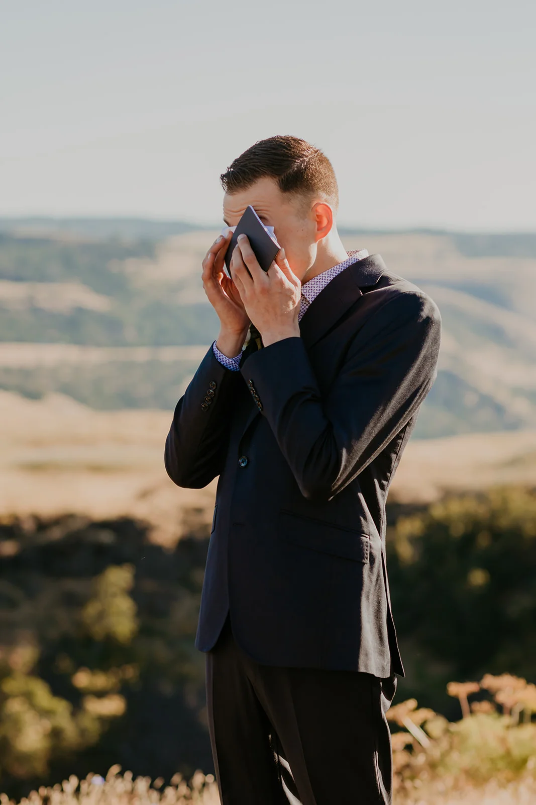 Nolan wipes away tears of joy in a navy suit at Mayer State Park in Mosier, OR, during his wedding to Ben.