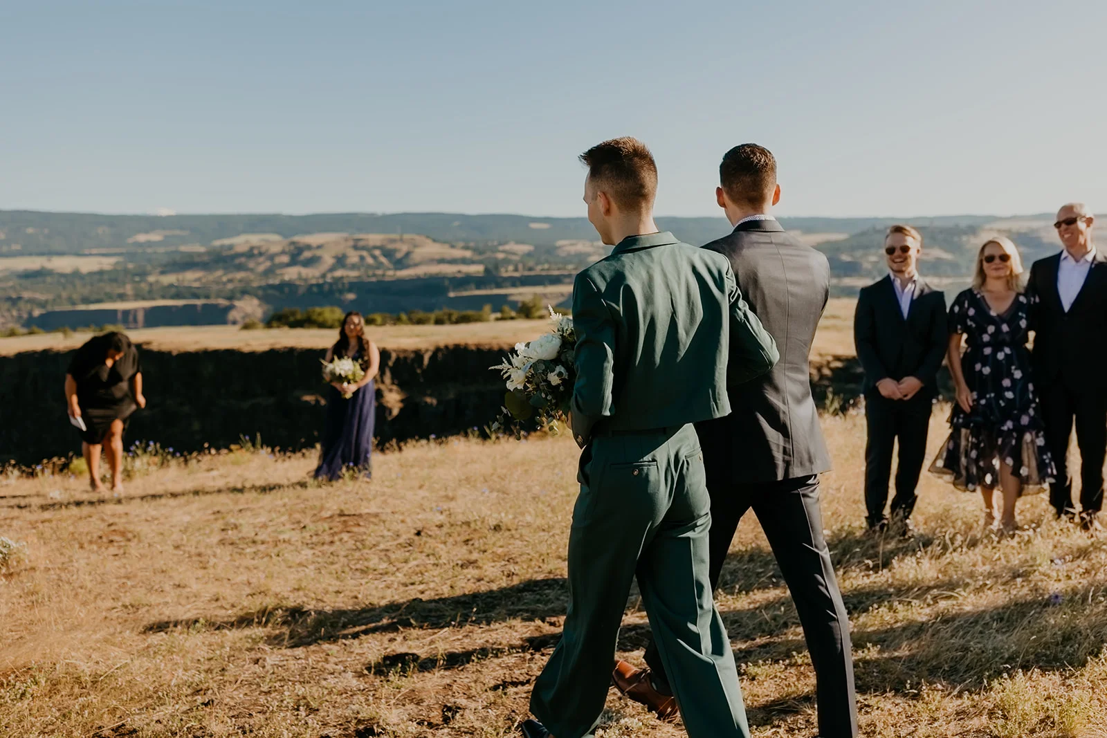 Ben and Nolan walk together holding white florals at their outdoor wedding at Mayer State Park in Mosier, OR.