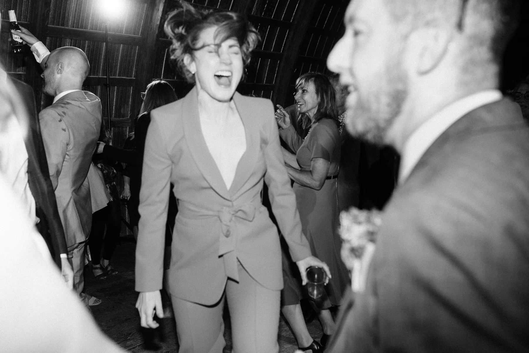 A guest in a tailored suit laughs and dances joyfully at Trent and Cameron Harris-McCoy's wedding reception at The Hillside Lodge.