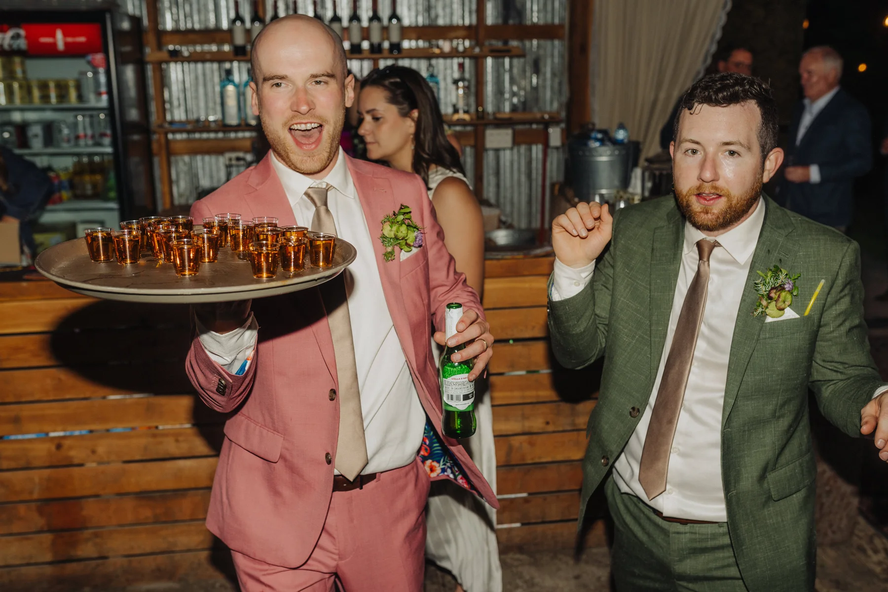 A groomsman in a pink suit carries a tray of shots at Trent and Cameron Harris-McCoy's wedding at The Hillside Lodge in Golden, BC.