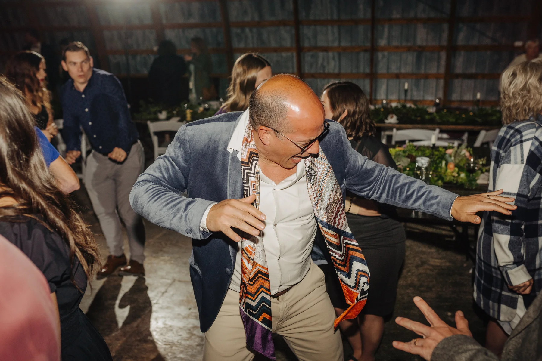 A guest dances energetically in a blue blazer and colorful scarf at The Hillside Lodge & Chalets wedding reception in Golden, BC.