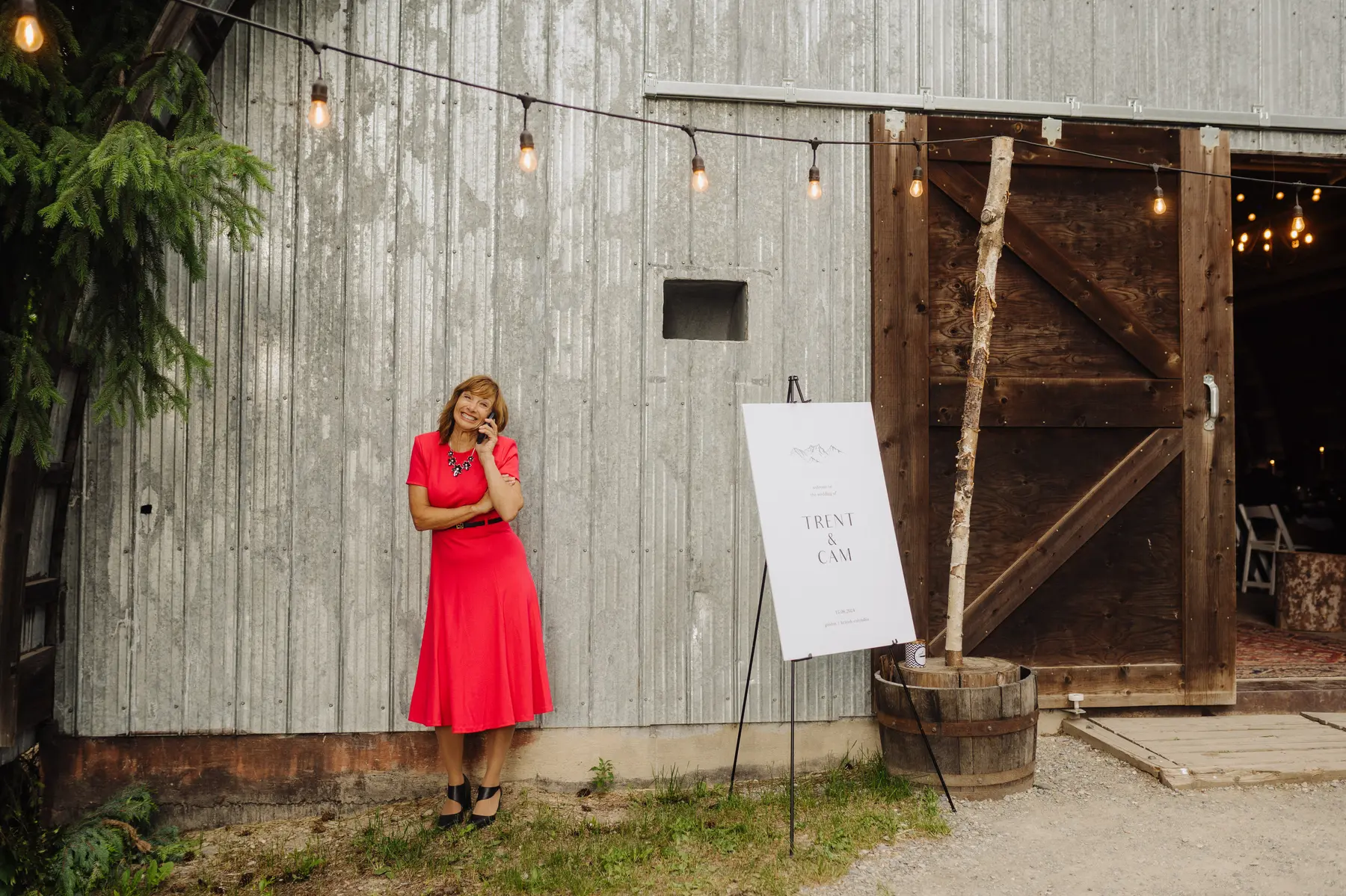 A wedding guest in a red dress talks on the phone outside The Hillside Lodge in Golden, BC, at Trent and Cam's wedding.
