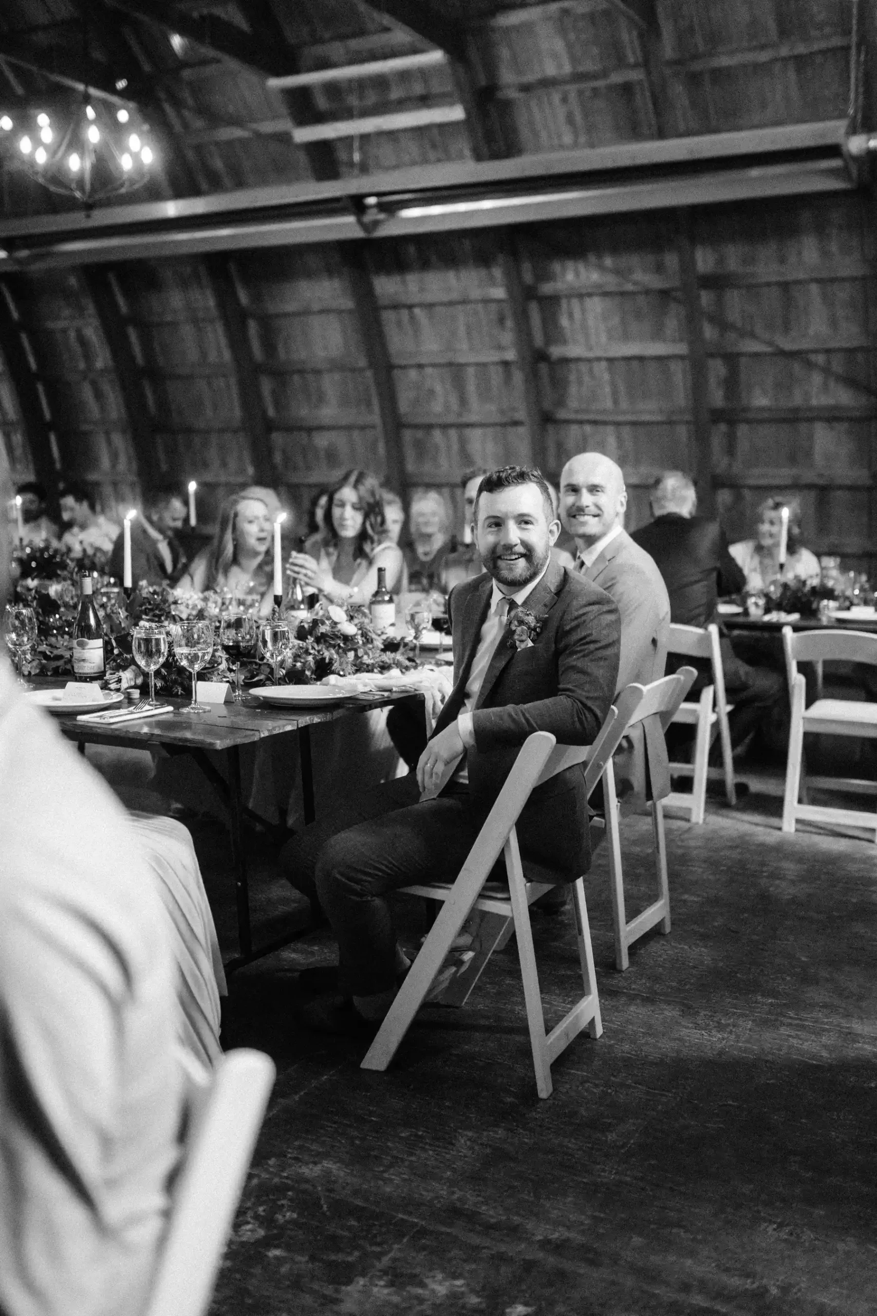 Groom Trent Harris-McCoy smiles at a barn reception table at The Hillside Lodge & Chalets in Golden, BC, Canada.
