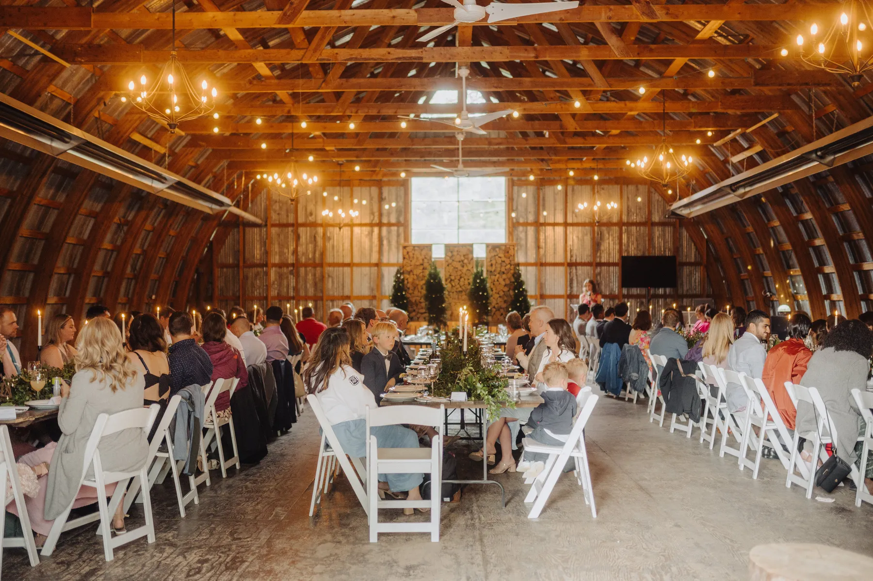 Wedding reception guests seated at long tables inside The Hillside Lodge & Chalets barn in Golden, BC, Canada.