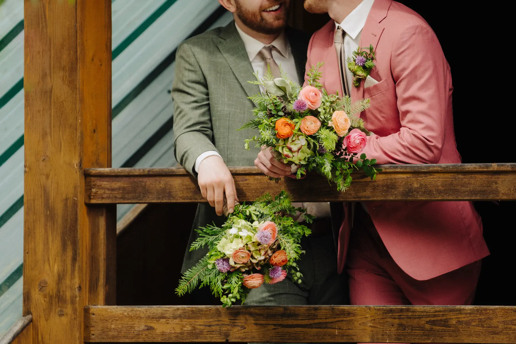 Trent and Cameron Harris-McCoy hold colorful floral bouquets on a wooden railing at The Hillside Lodge in Golden, BC.