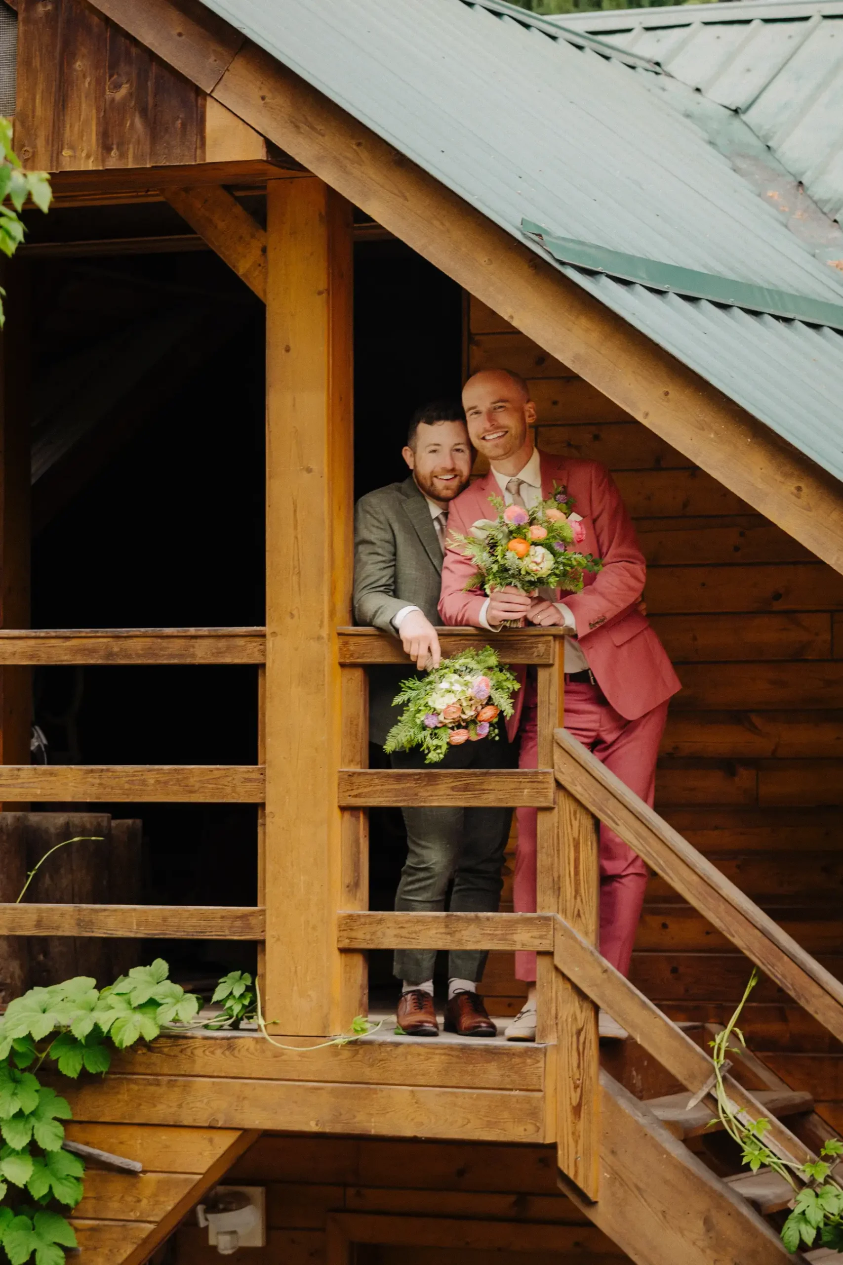 Trent and Cameron Harris-McCoy smile on a wooden balcony at The Hillside Lodge & Chalets, holding colorful bouquets.