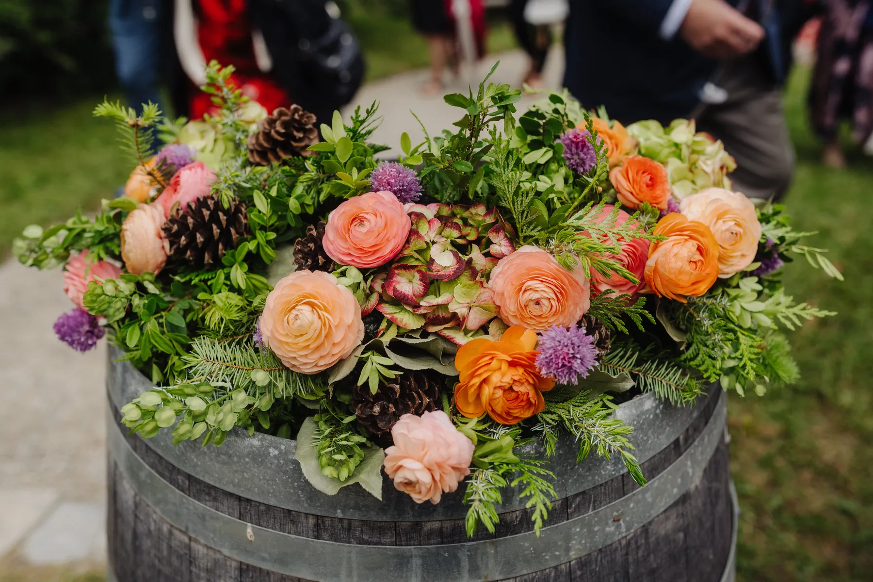 Lush floral arrangement of peach ranunculus, orange roses, purple allium and pine cones atop a wine barrel at The Hillside Lodge & Chalets.