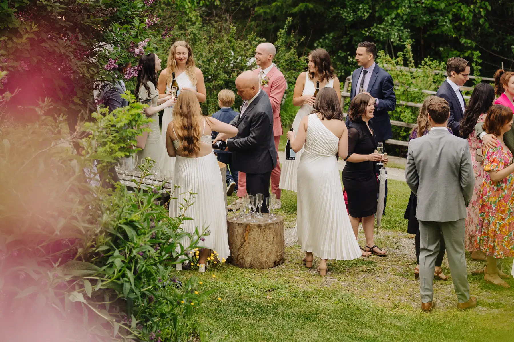 Wedding guests mingle outdoors at The Hillside Lodge & Chalets in Golden, BC, as champagne is poured on a tree stump.