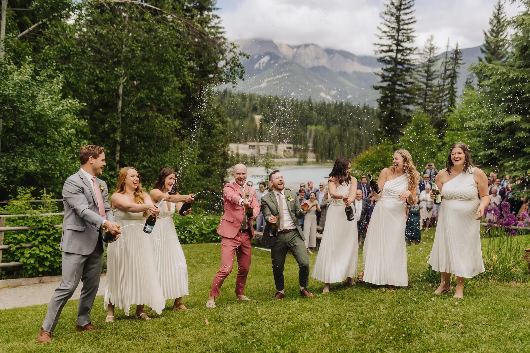 Trent and Cameron Harris-McCoy spray champagne with their wedding party on the lawn at The Hillside Lodge & Chalets in Golden, BC.