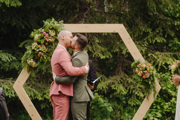 Trent and Cameron Harris-McCoy share their first kiss as spouses under a hexagonal wood arch at The Hillside Lodge & Chalets in Golden, BC.