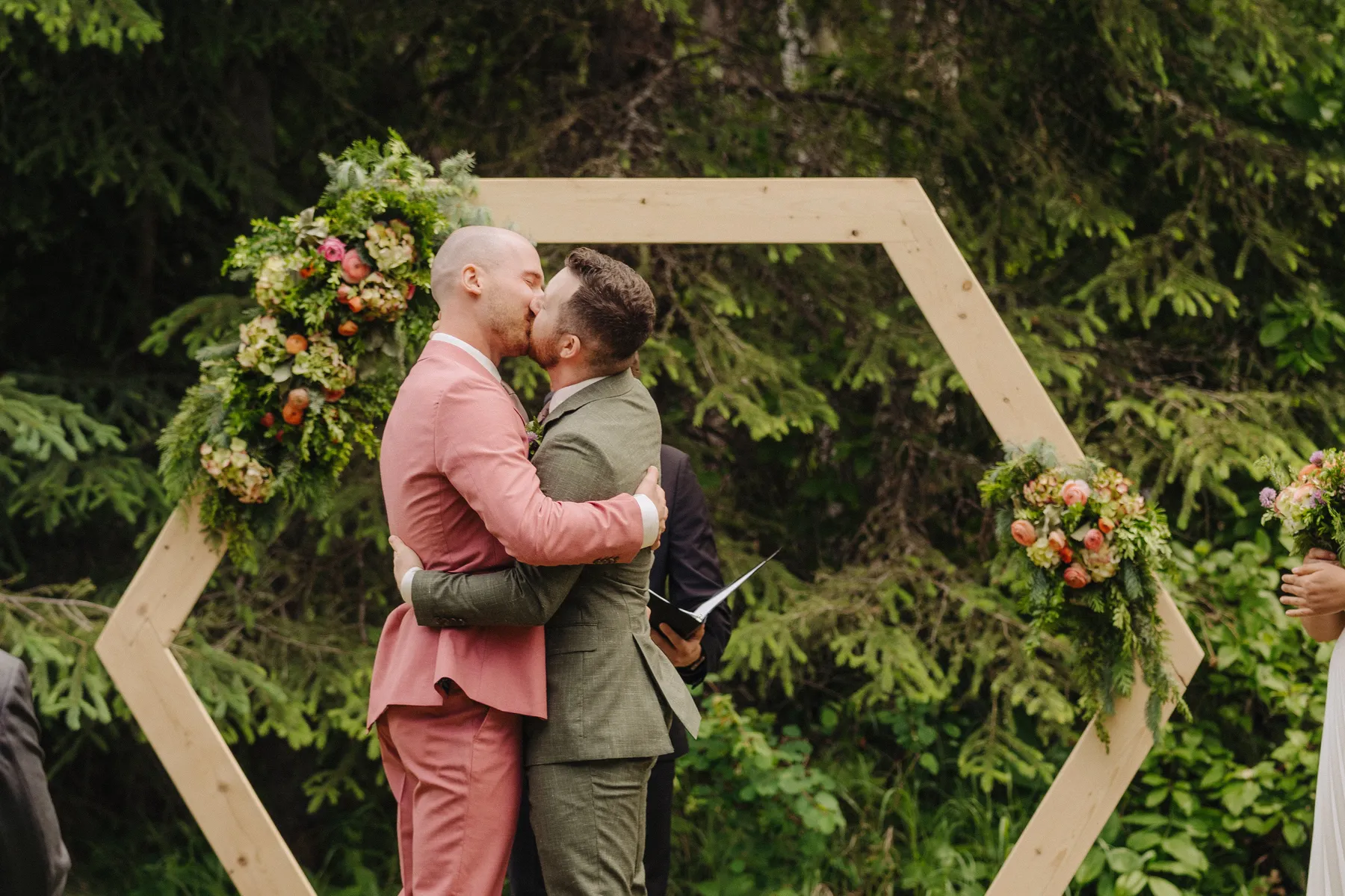 Trent and Cameron Harris-McCoy share their first kiss as spouses under a hexagonal wood arch at The Hillside Lodge & Chalets in Golden, BC.