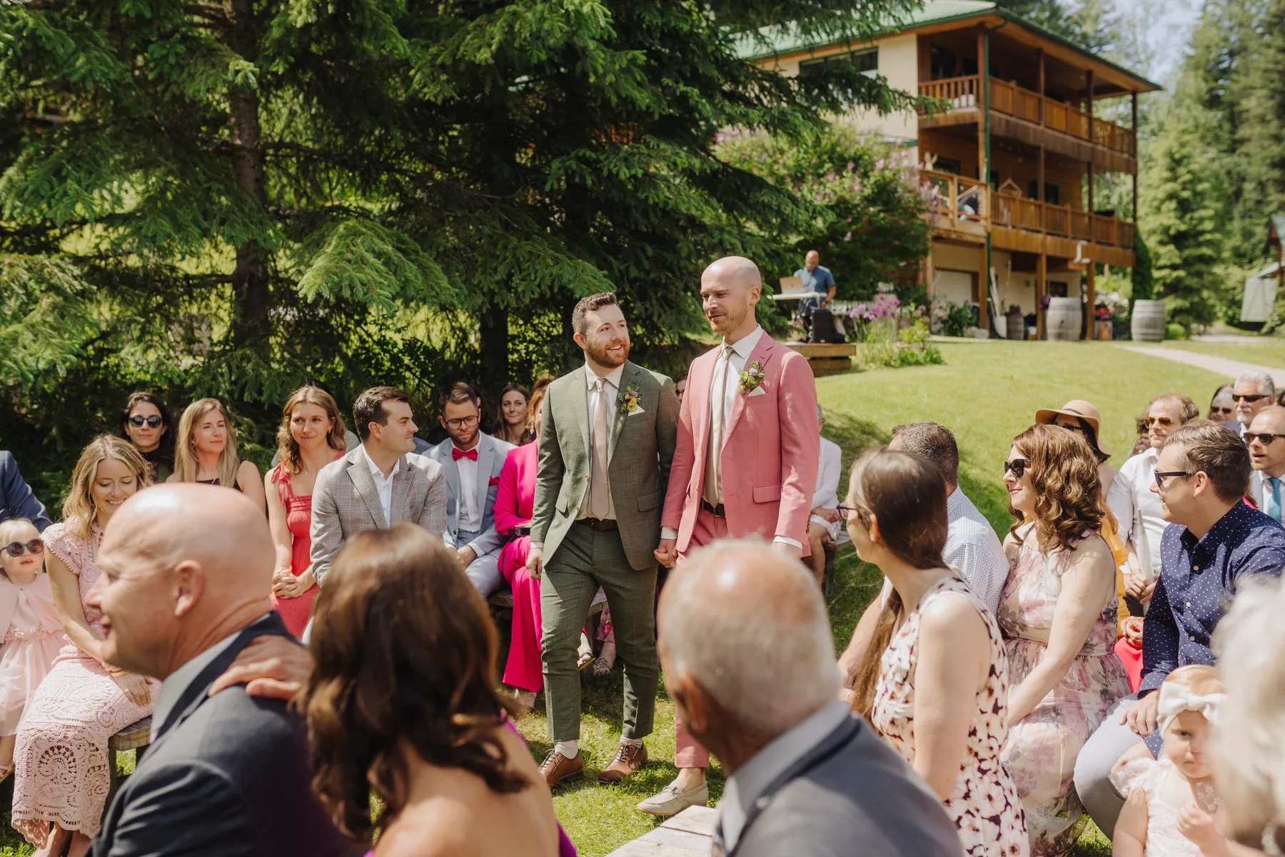 Grooms Trent and Cameron Harris-McCoy hold hands walking the aisle at The Hillside Lodge & Chalets in Golden, BC.