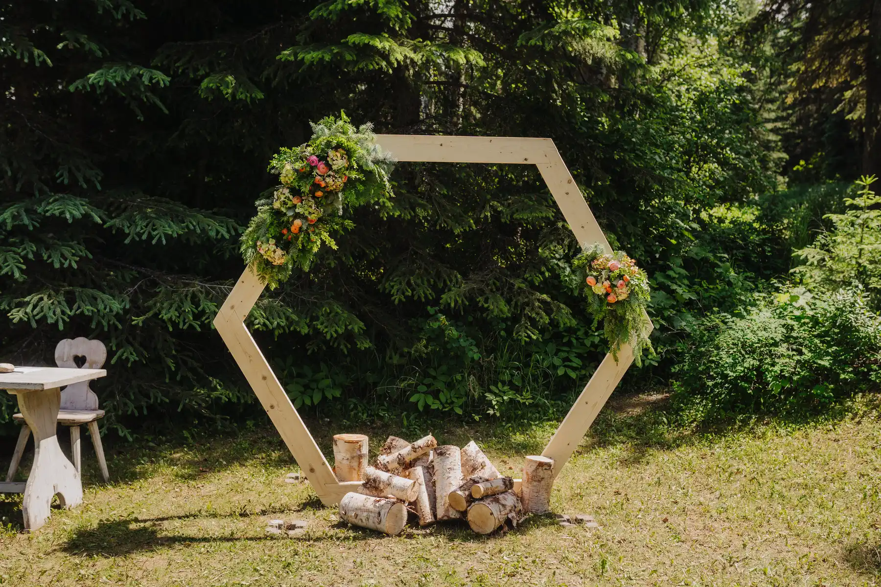Hexagonal wooden wedding arch adorned with colorful florals and birch logs at The Hillside Lodge & Chalets in Golden, BC.