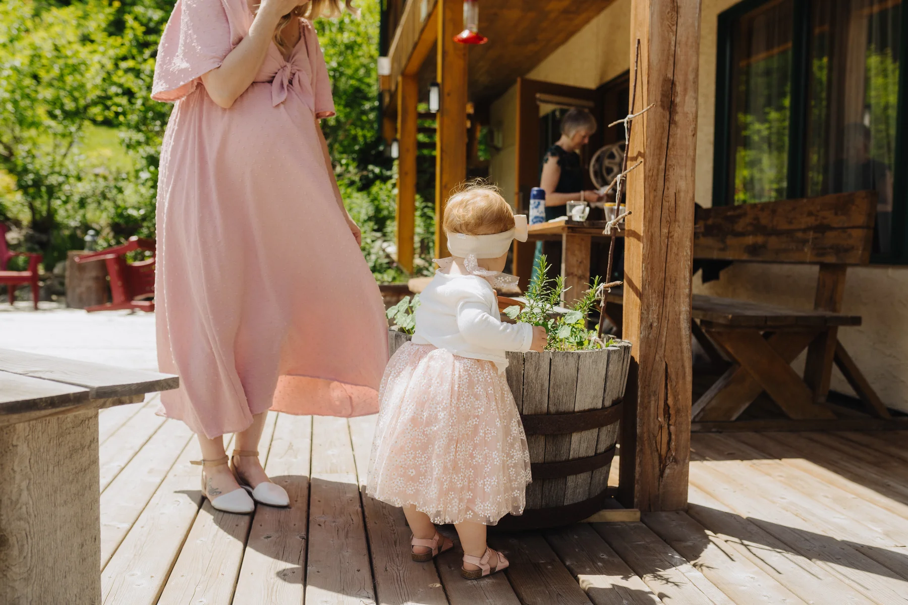 A toddler in a pink skirt explores a wooden barrel planter on the deck at The Hillside Lodge & Chalets in Golden, BC.