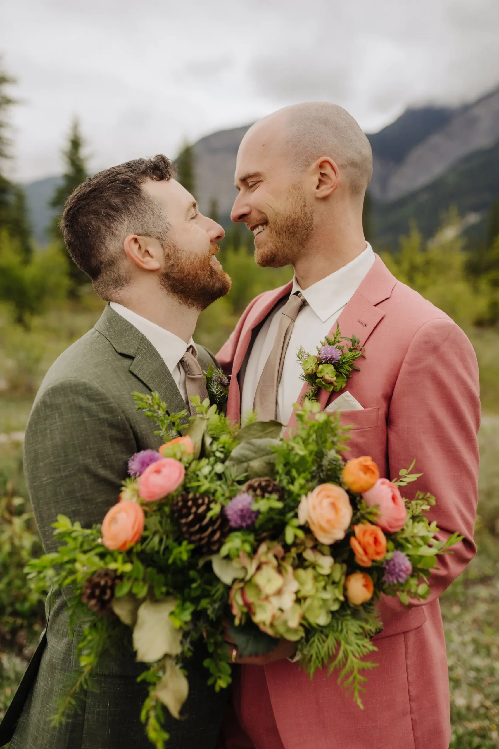 Trent and Cameron Harris-McCoy share a tender moment in matching boutonnieres and colorful floral bouquet at The Hillside Lodge, Golden, BC.