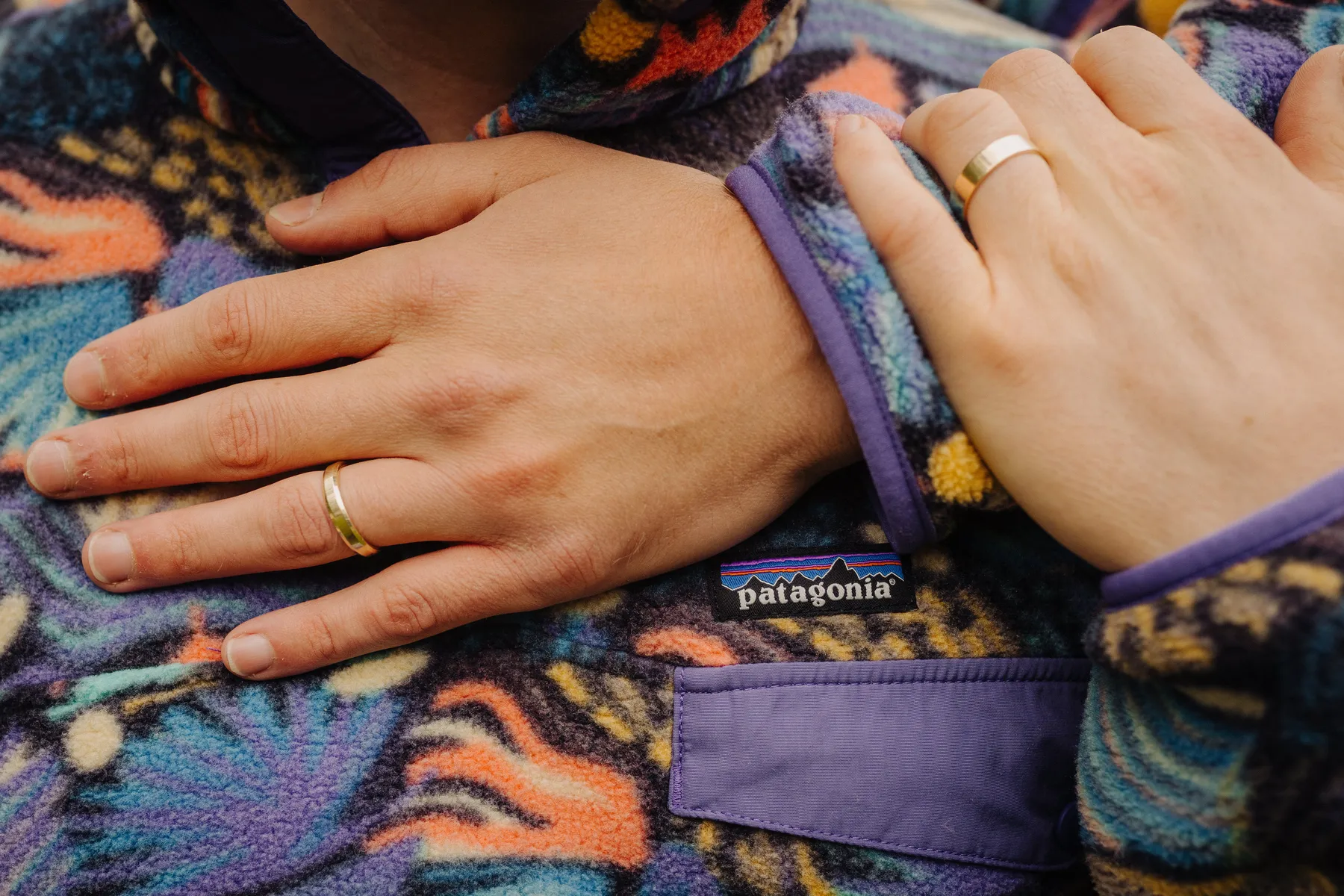 Trent and Cameron Harris-McCoy rest their hands together, both wearing gold wedding bands, on a colorful Patagonia fleece.
