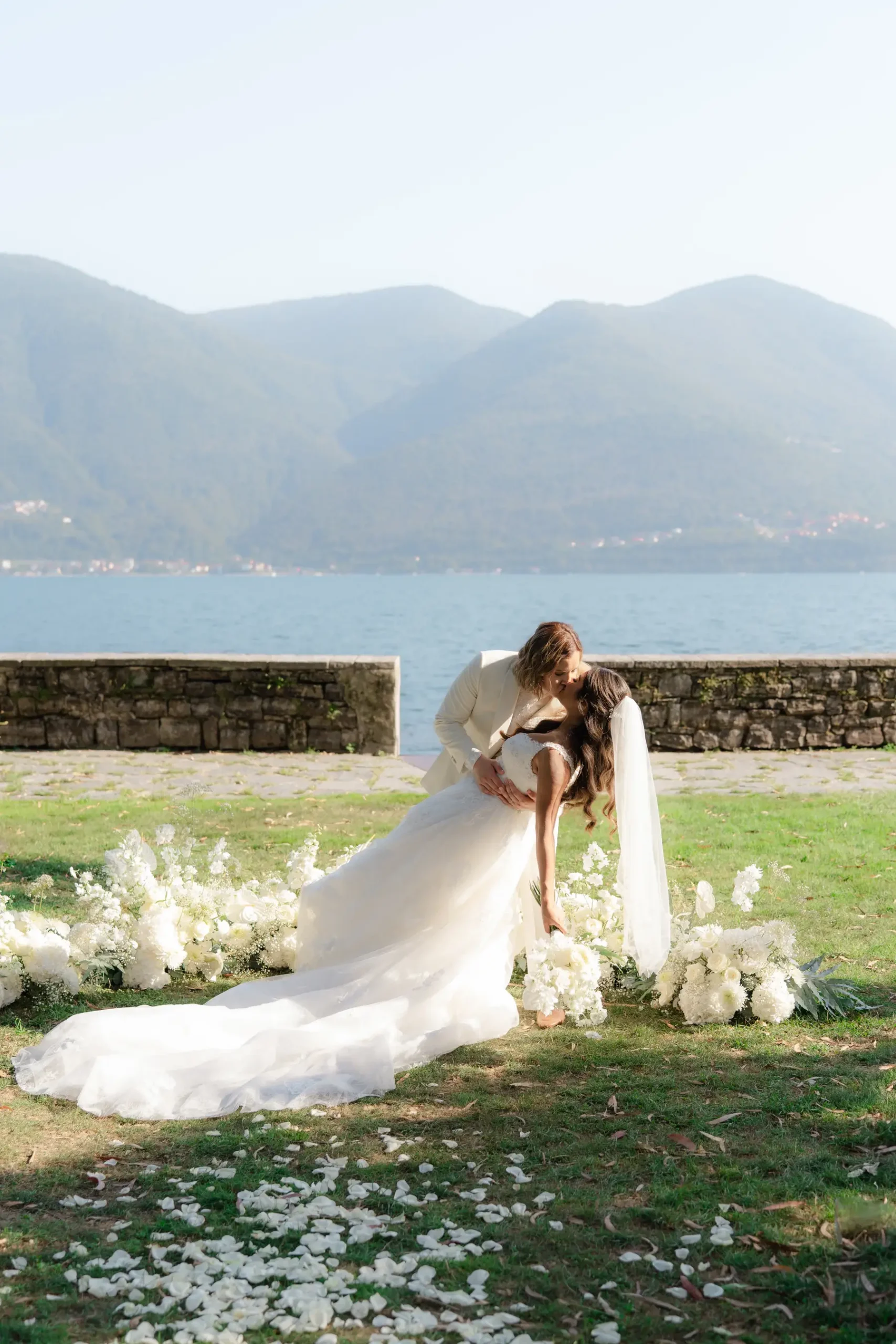 Ashley and Dionne share a dip kiss amid white floral arrangements at Villa Emden on Brissago Island, Switzerland.
