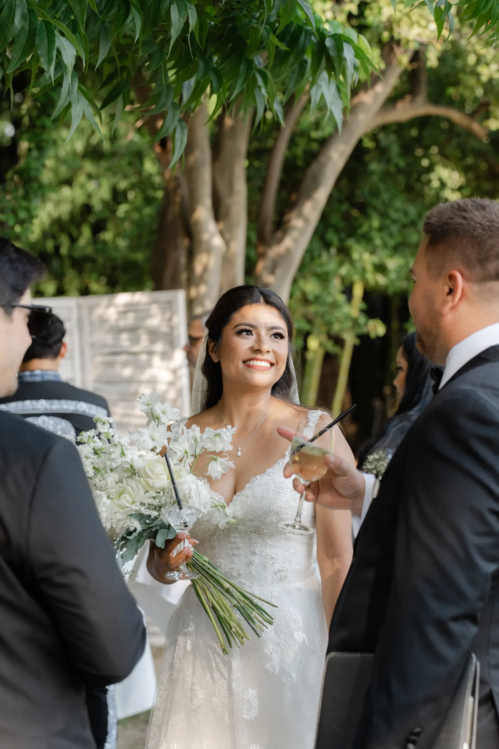 Bride Ashley Rodriguez-Vargas smiles joyfully holding white bouquet and champagne glass at Villa Emden, Brissago Island, Switzerland.
