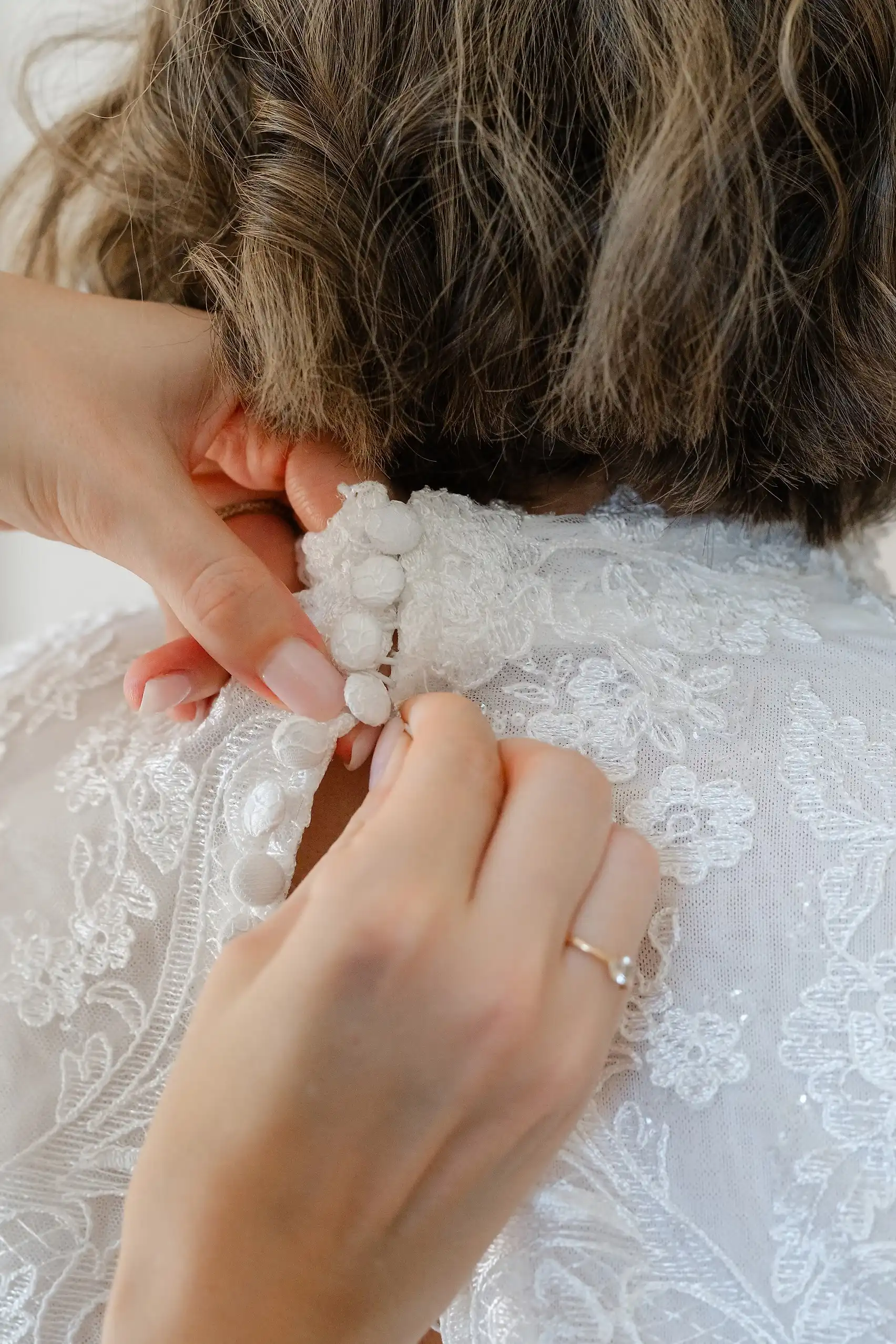Hands fastening fabric buttons on the back of a lace wedding dress at Villa Emden, Brissago Island, Switzerland.